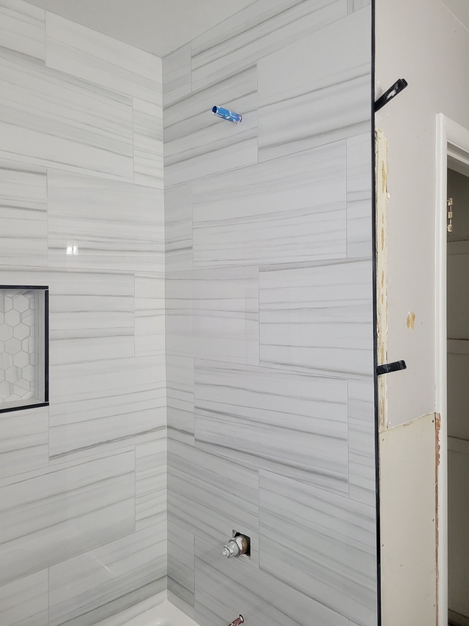 Tiled shower stall with a niche and exposed plumbing fixtures, mid-installation.