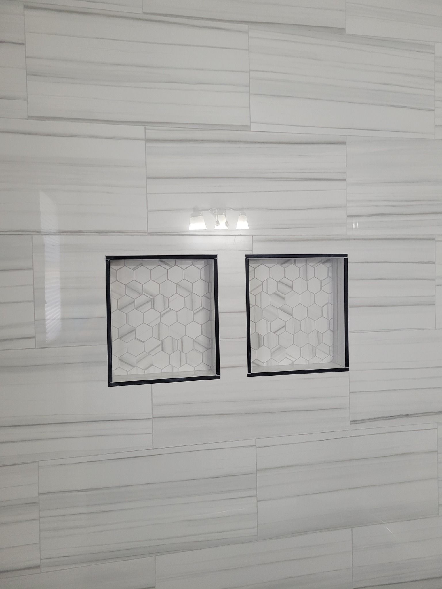 Two small square windows with white curtains set in a light tiled wall.