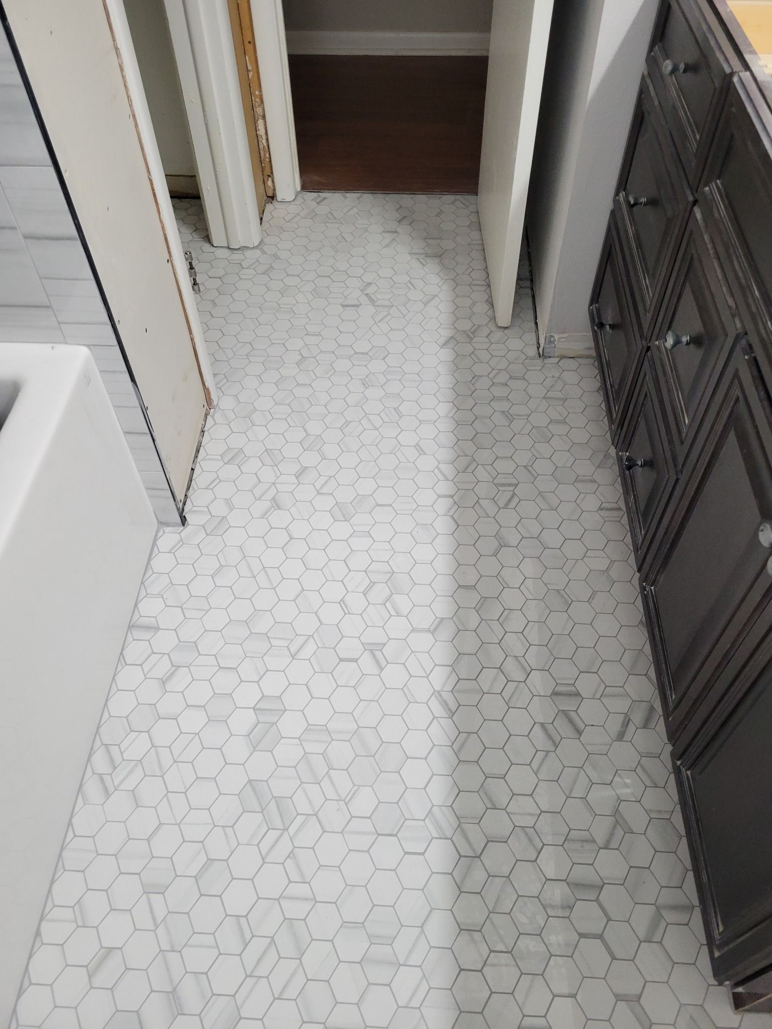 Narrow tiled hallway with white patterned floor, a doorway ahead, and dark storage cabinets on the right.