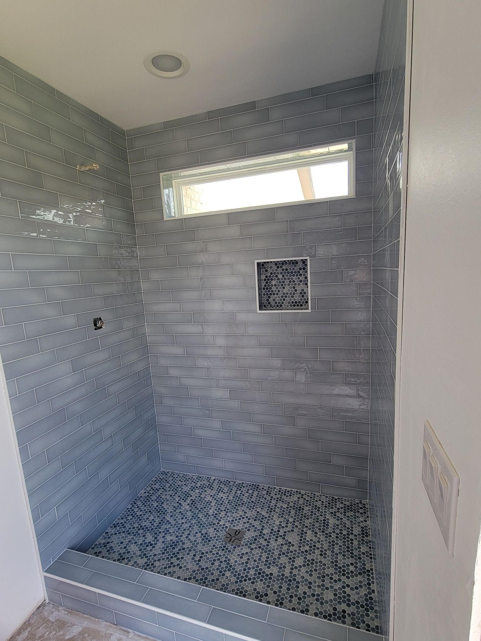 Tiled walk-in shower with pebble floor, small high window, and built-in wall niche.