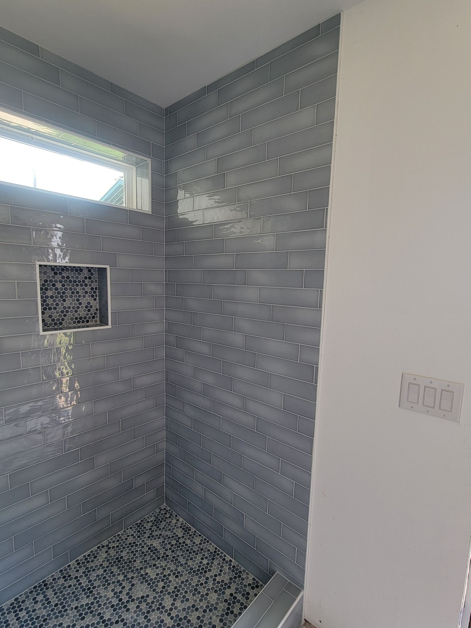 Small tiled shower stall with gray walls, a window, and a drain on the floor.