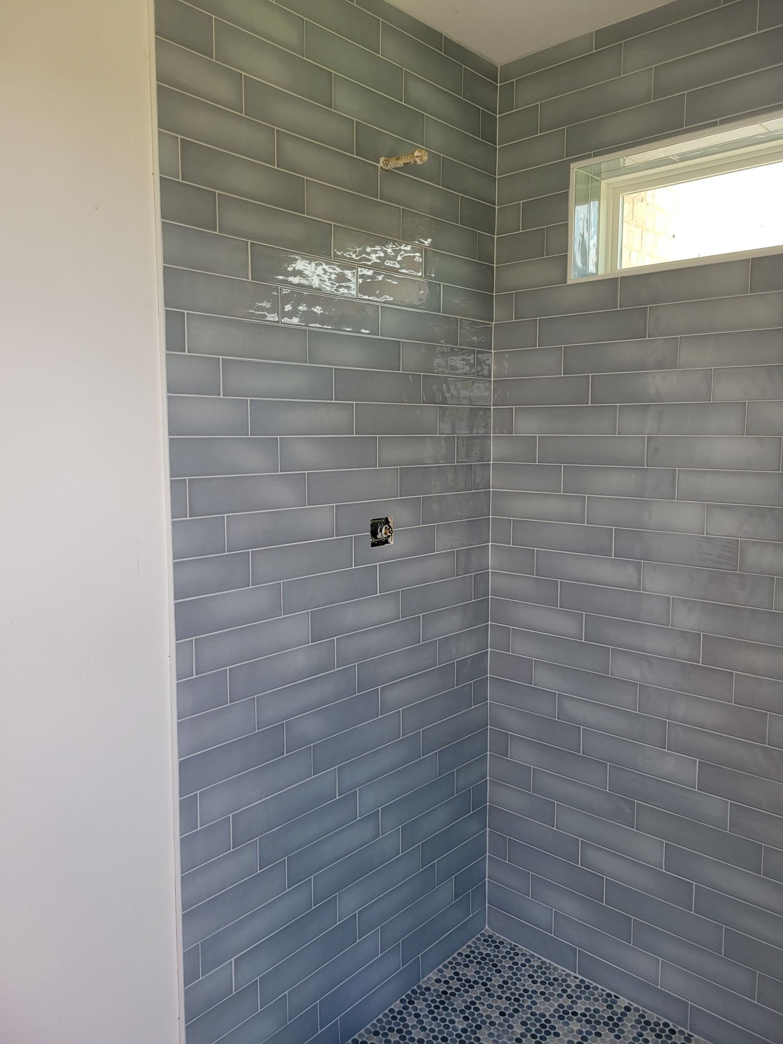 Tiled shower corner with gray subway tiles and a small window, unfinished with exposed screw points