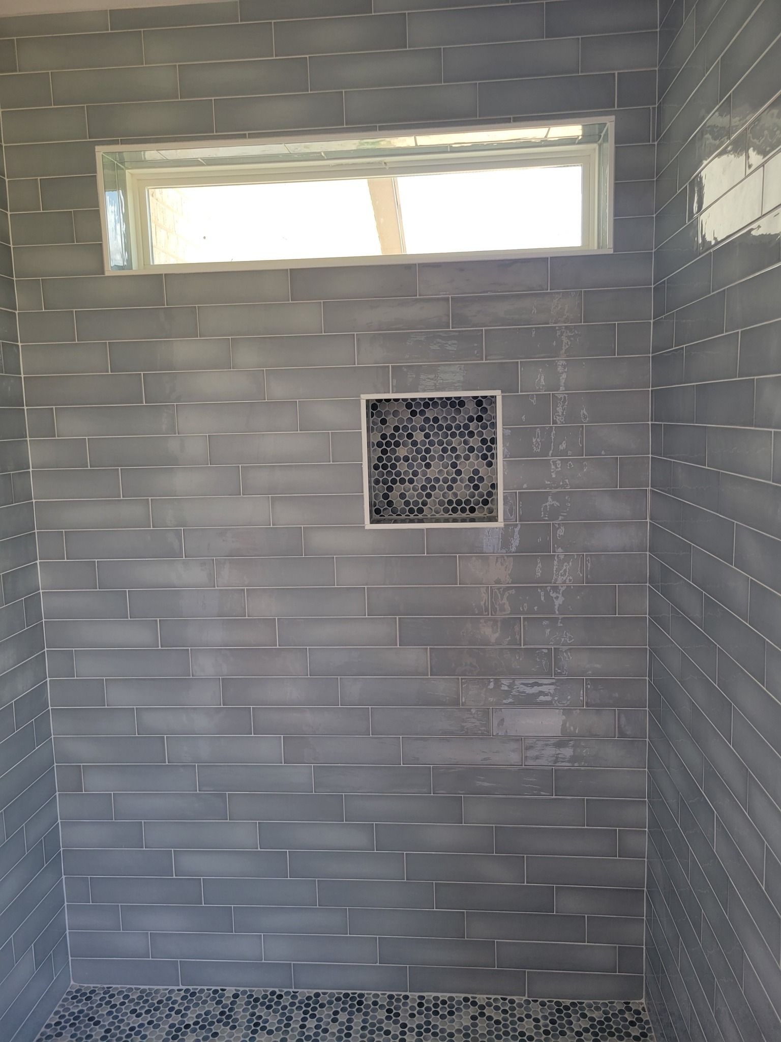 Gray-tiled shower stall with a small window and square vent on the back wall.