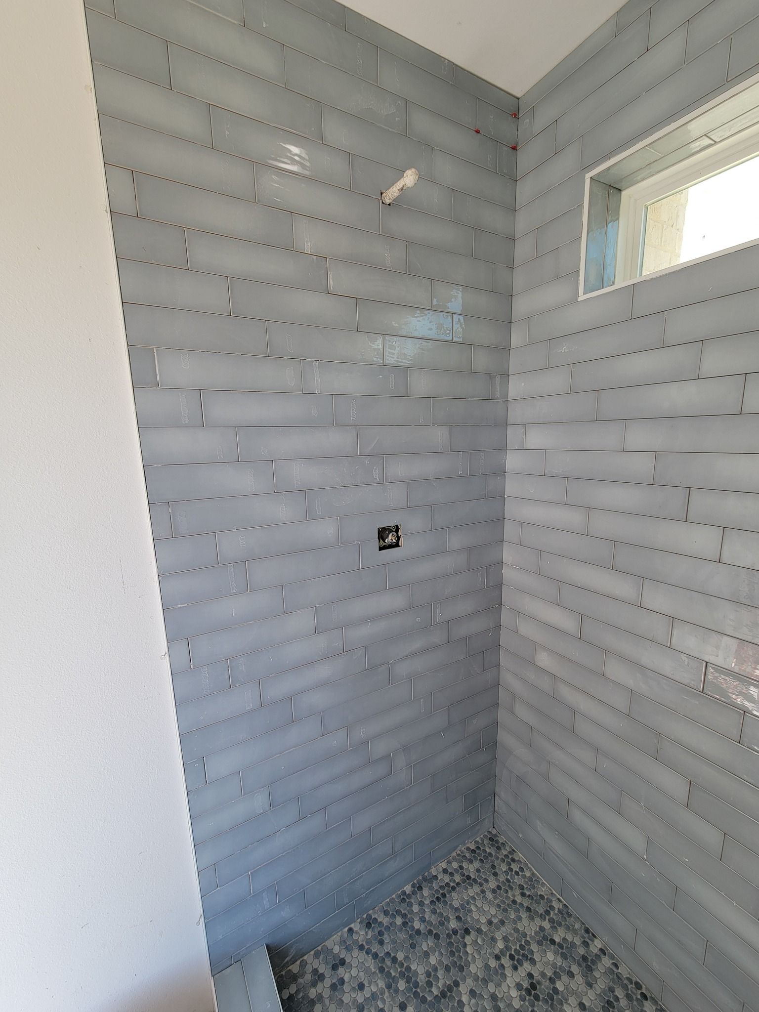 Small tiled bathroom shower stall with gray walls, white mosaic floor, and a small window.