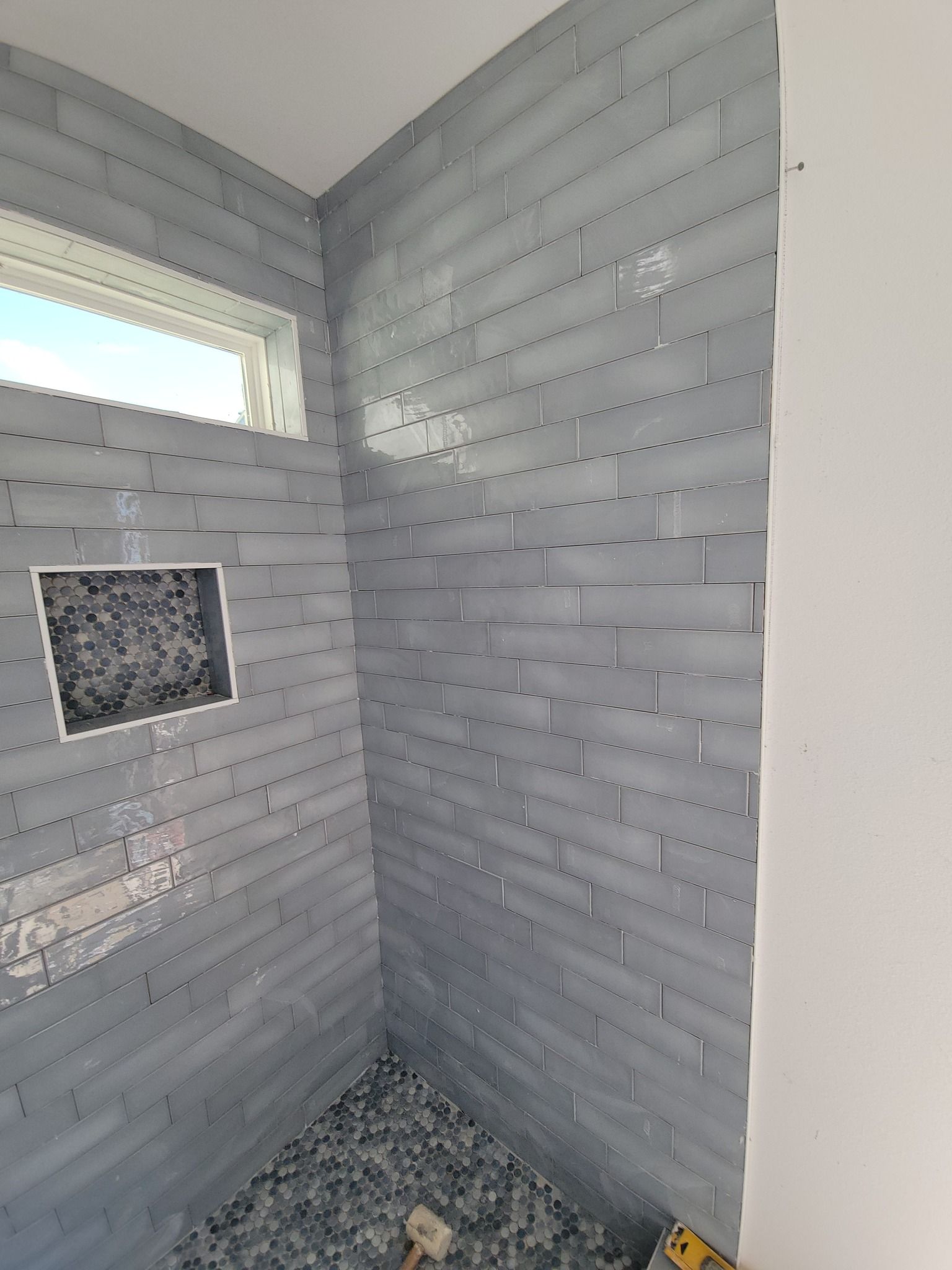Small tiled shower stall with gray walls, a small window, and a recessed shelf.