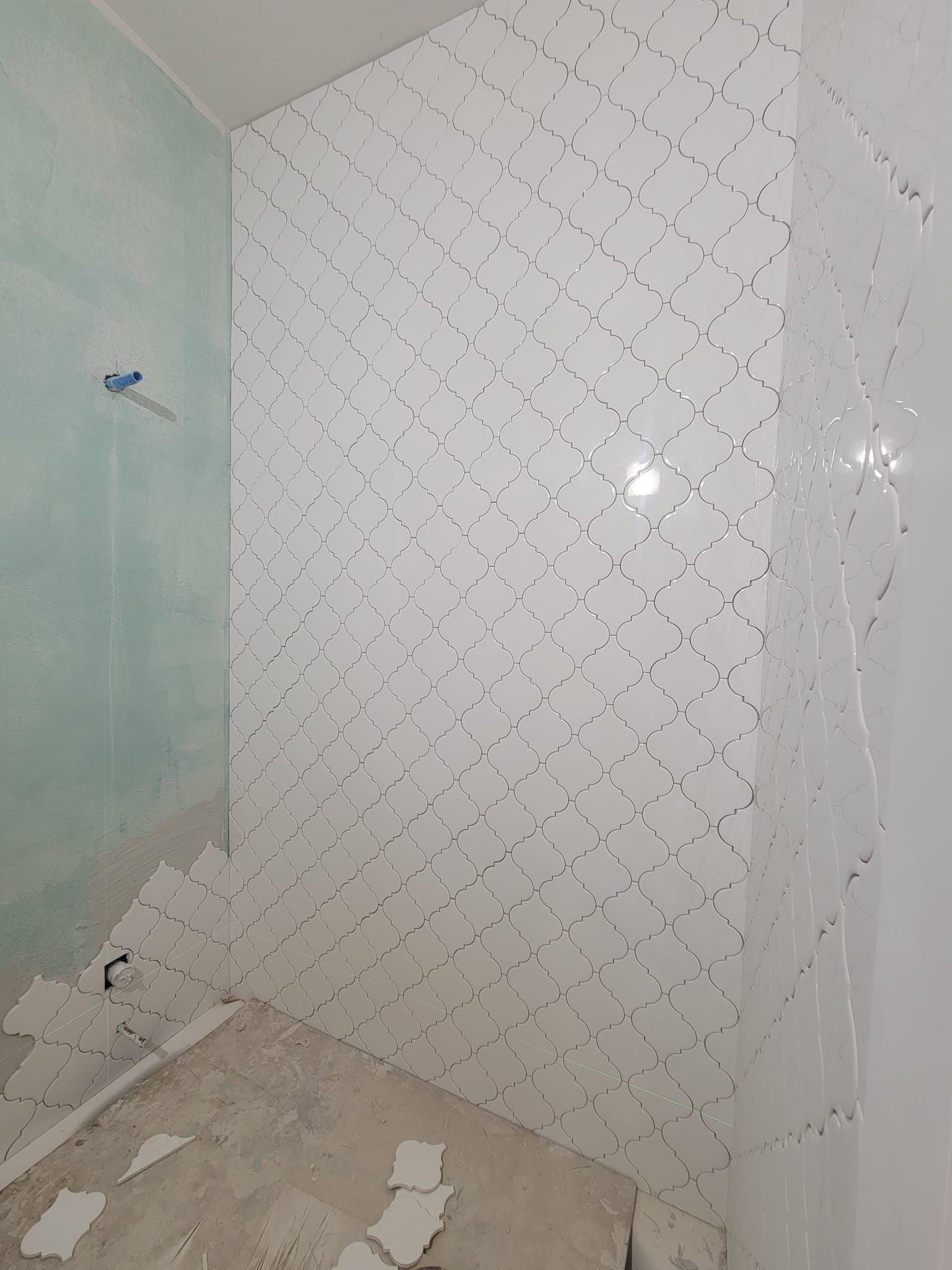 Partially tiled bathroom wall with white patterned tiles and bare floor during renovation