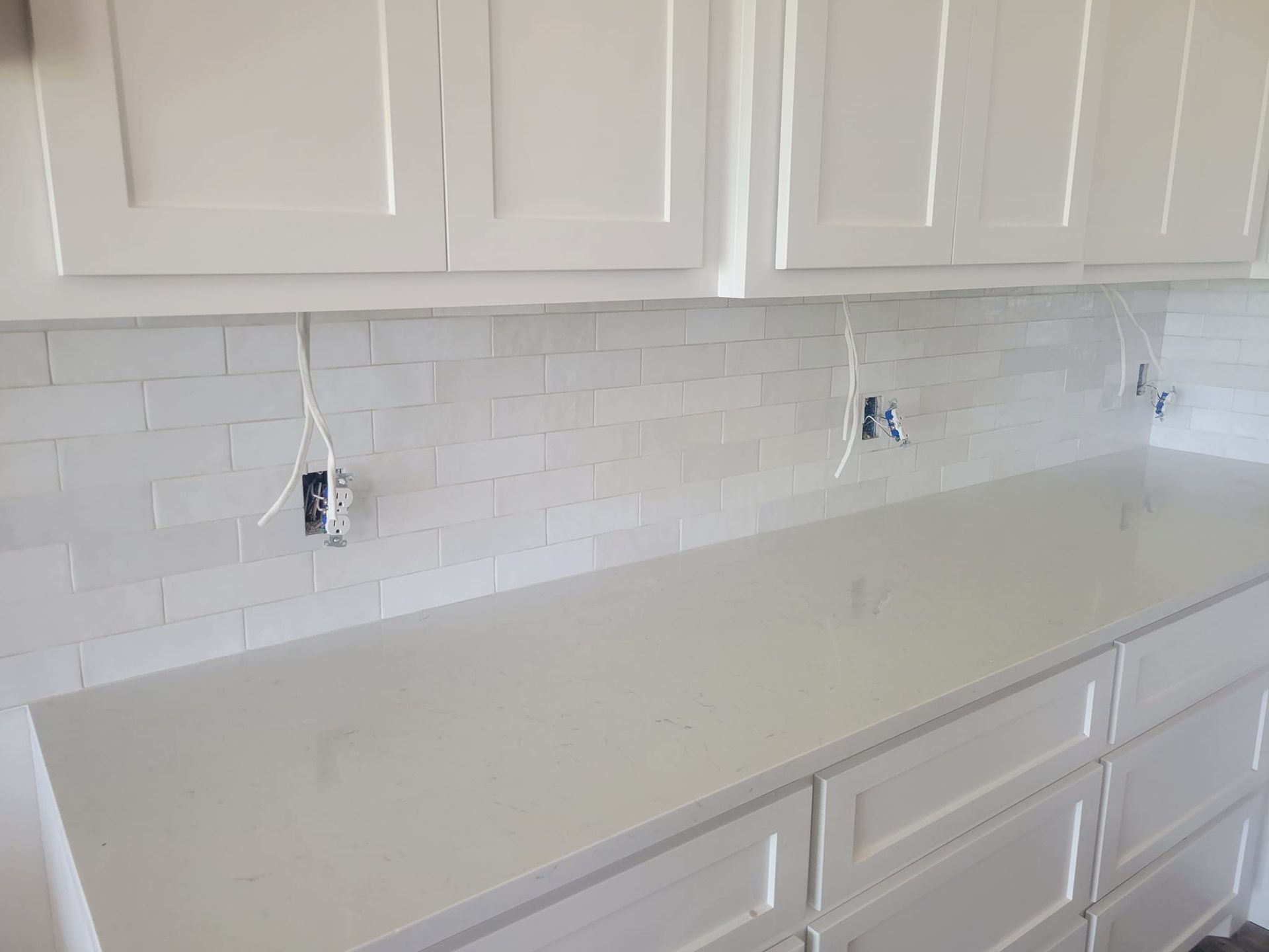 White kitchen countertop with white cabinets and subway tile backsplash, showing two exposed outlets.