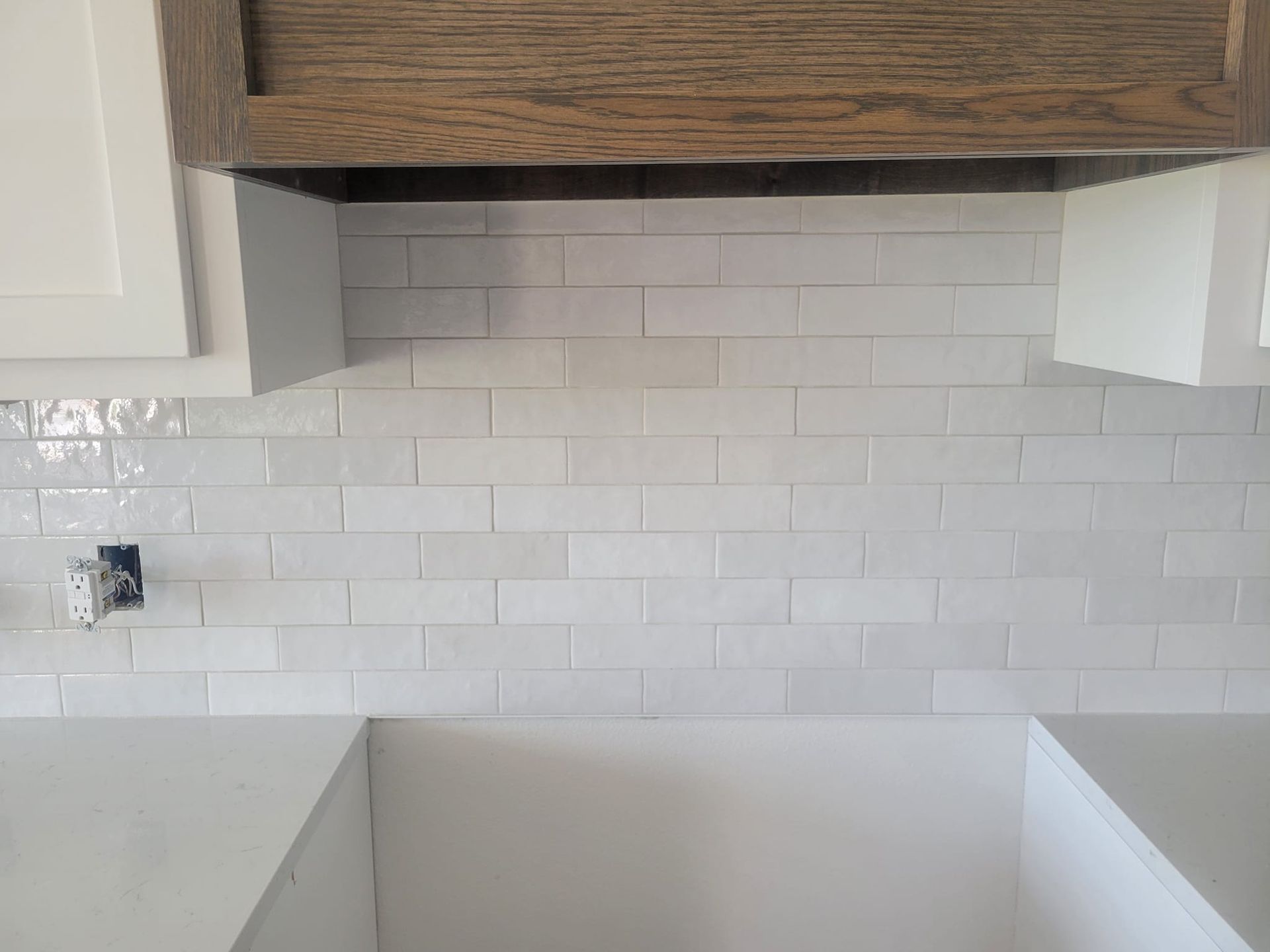 Empty kitchen backsplash with white subway tiles, wood range hood, and unfinished countertop area