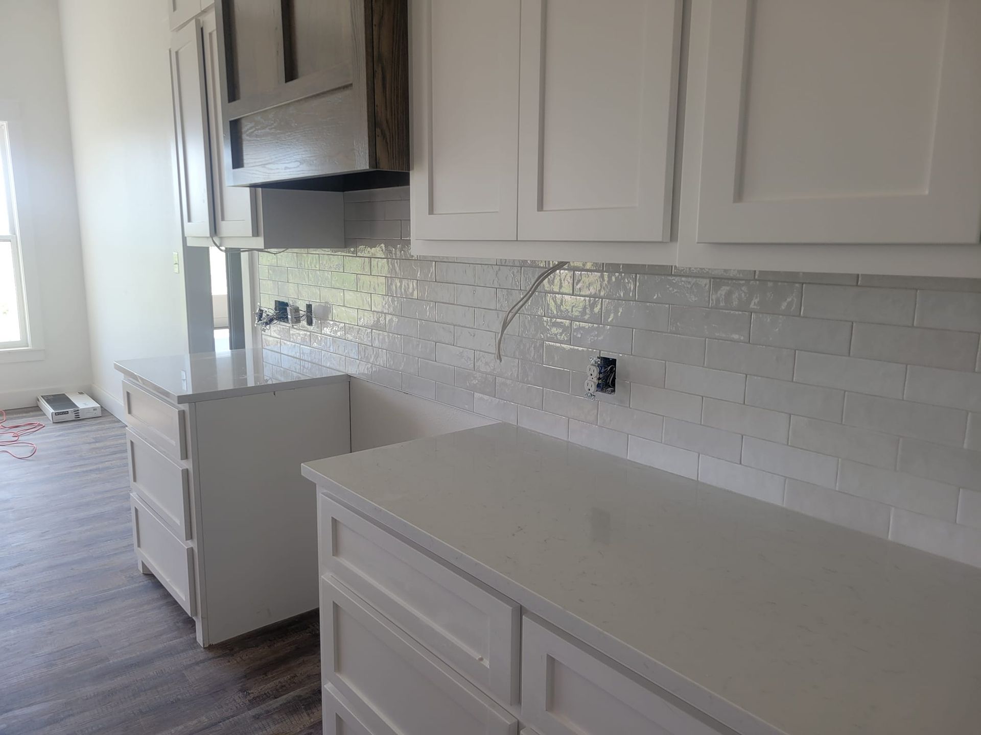 Bright kitchen with white cabinets, glossy countertops, and a subway tile backsplash; doorway to adjacent room.