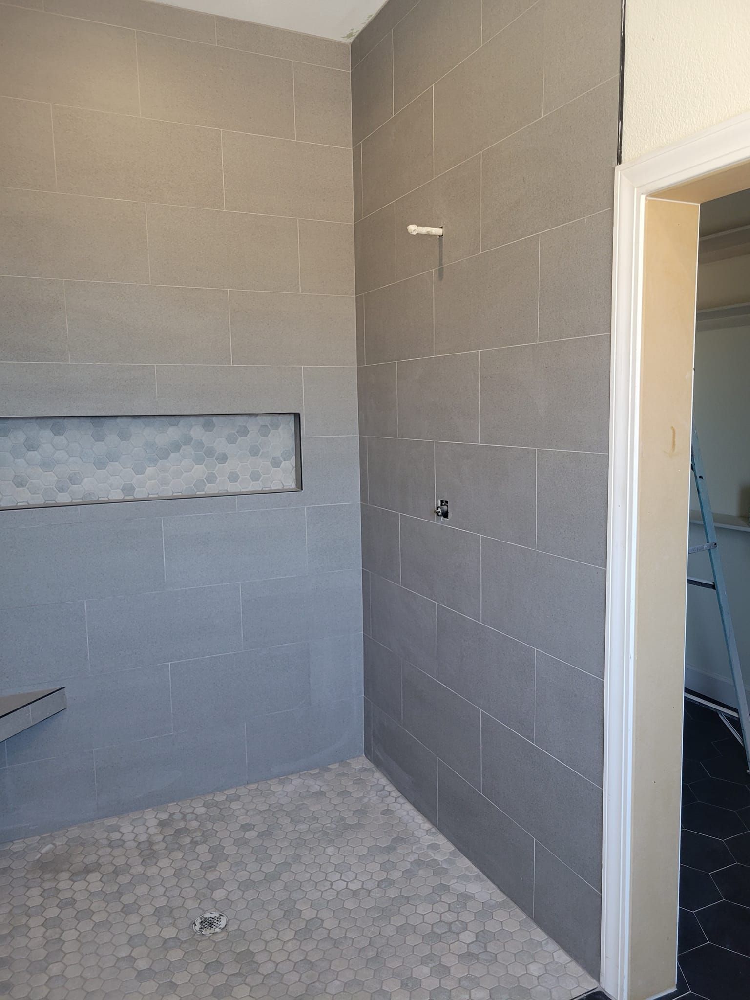 Small unfinished bathroom with gray tile walls, a recessed niche, and an open doorway.