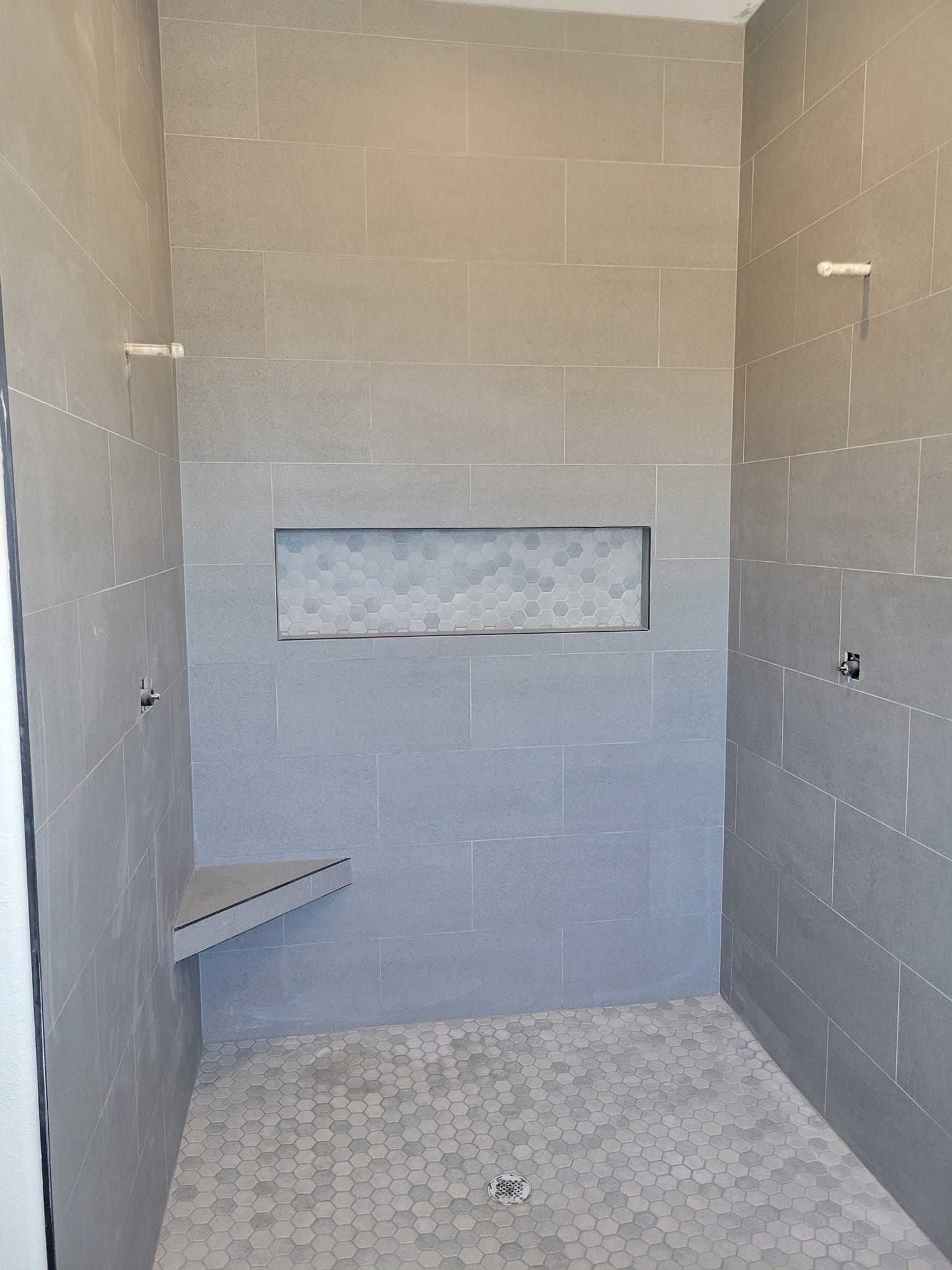 Gray tiled shower stall with built-in bench and recessed shelf.