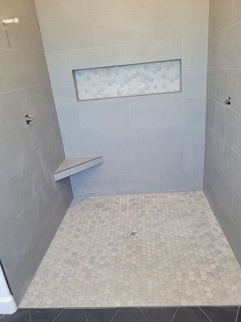 Tiled shower stall with built-in bench and recessed niche, empty and unfinished look