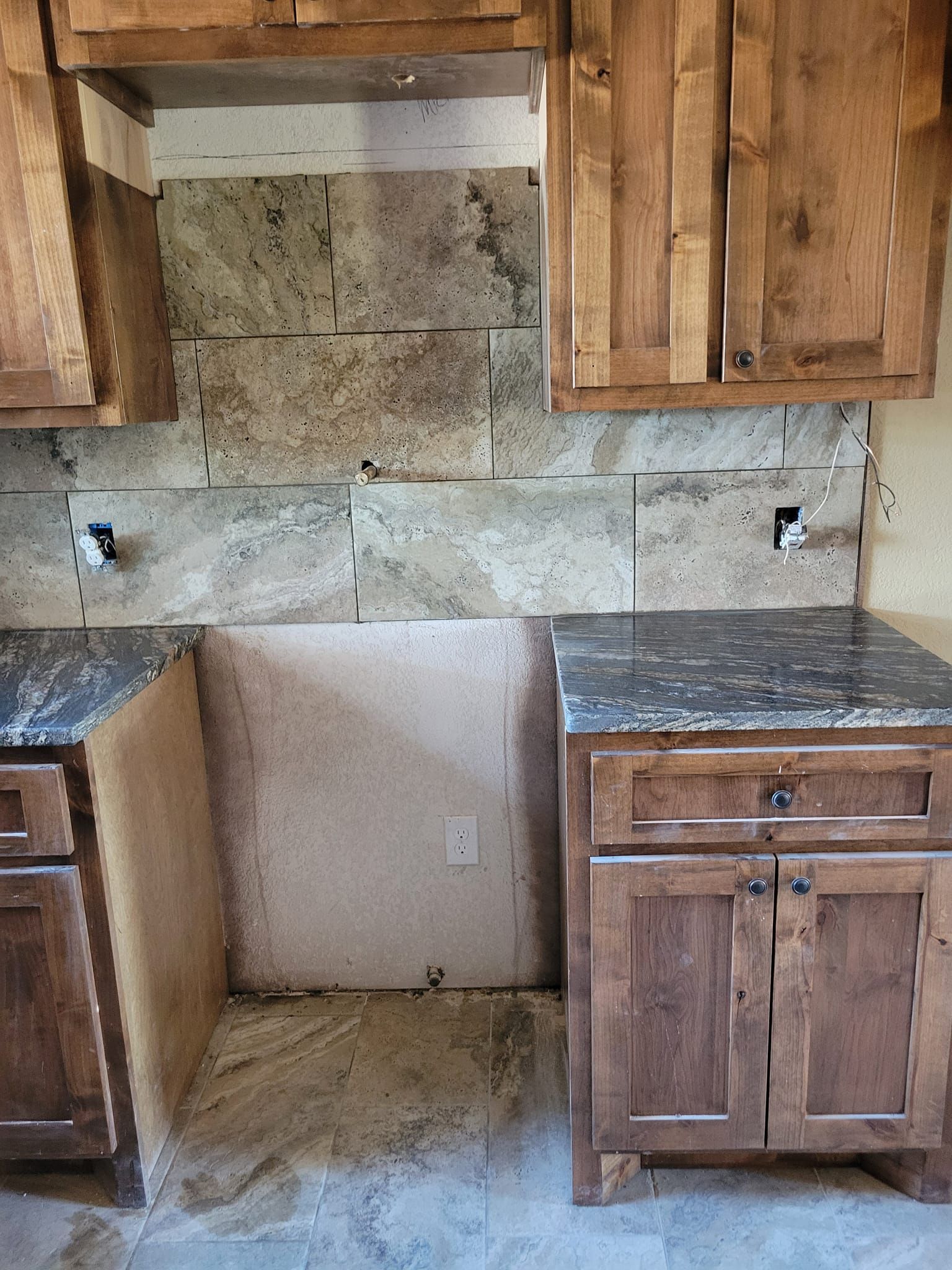 Empty kitchen area with wooden cabinets and granite countertops around a centered backsplash opening.