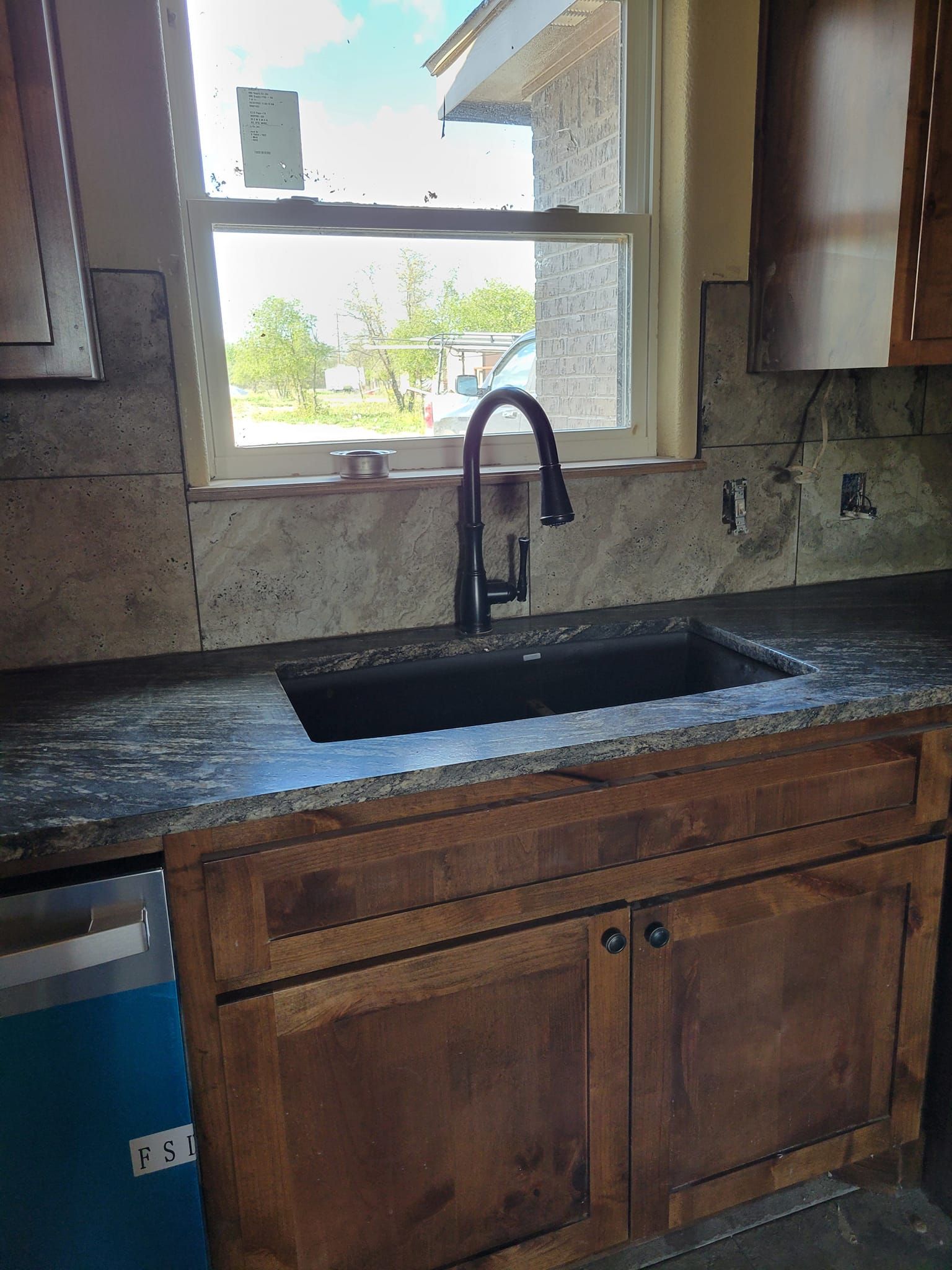 Kitchen sink beneath a window with a black faucet and wooden cabinets