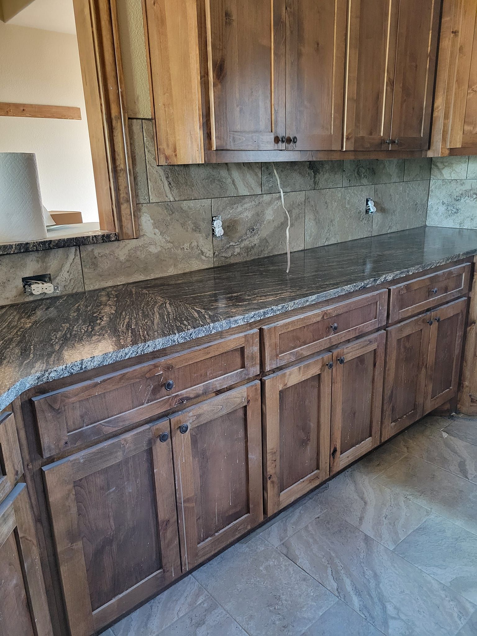 Wooden bathroom vanity with dark granite countertop, backsplash, mirror, and cabinets.