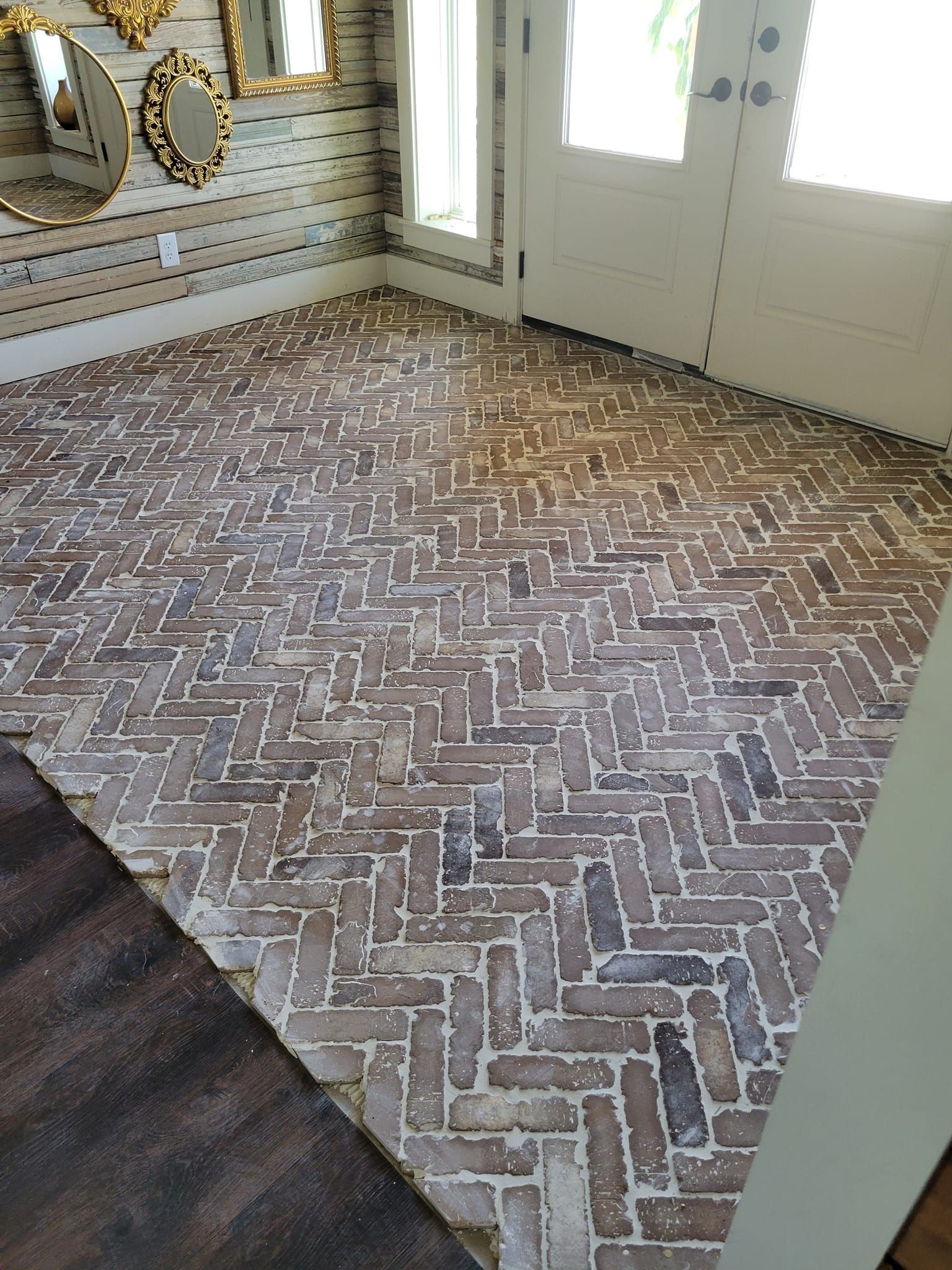 Brick-pattern floor near a white front door, with a dark rug and mosaic accent wall in the entryway