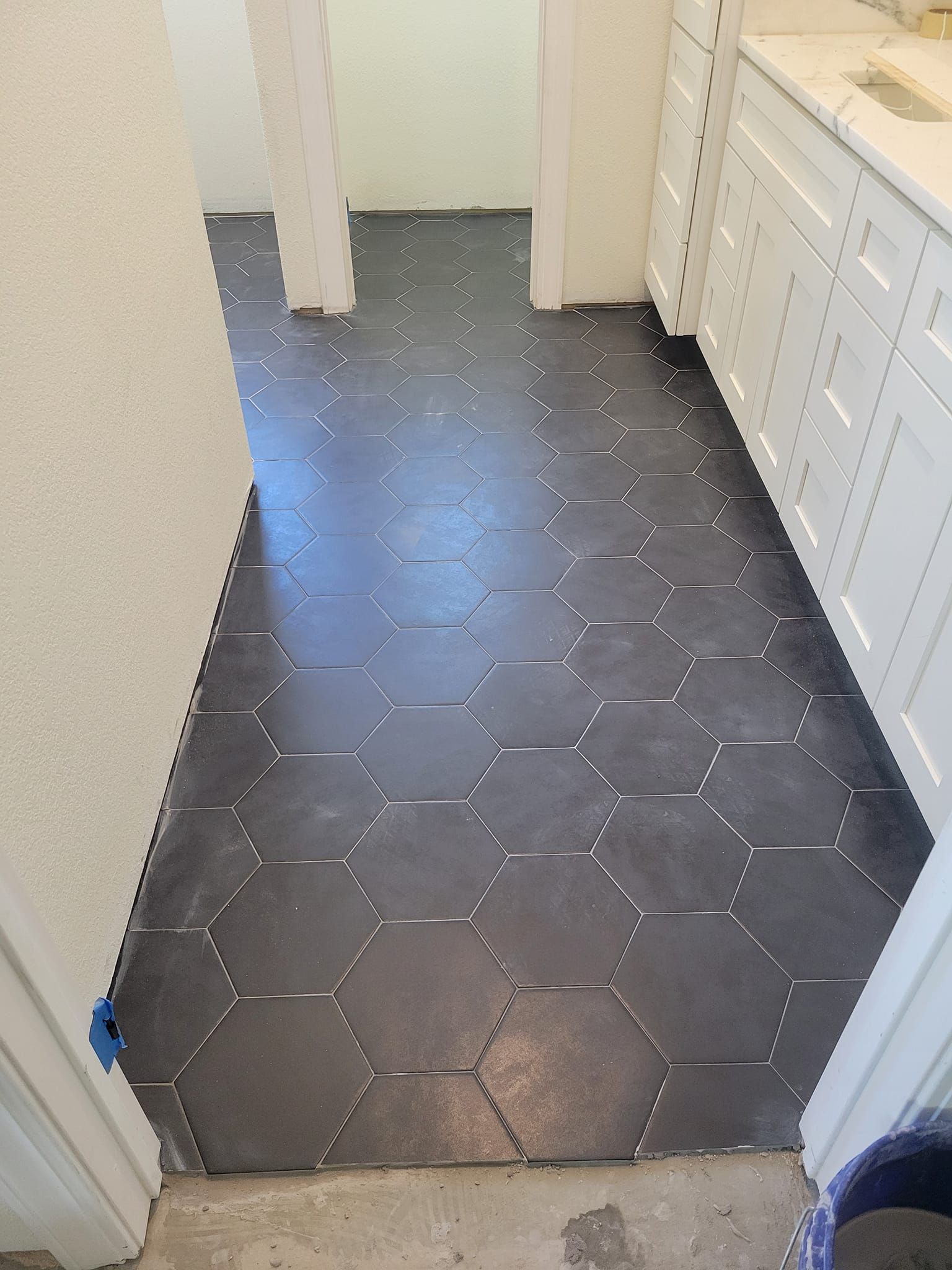 Narrow kitchen hallway with dark hex tile floor and white cabinets along the right wall.