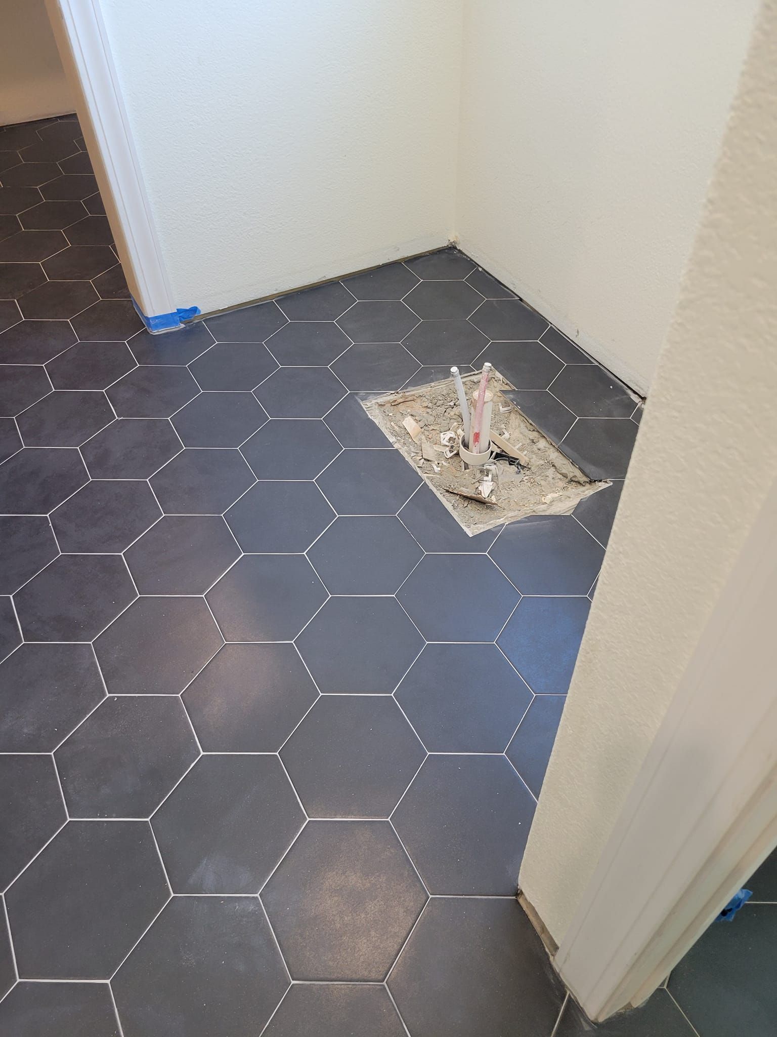 Hallway with dark hex tile floor and a damaged patch exposing debris near a doorway.