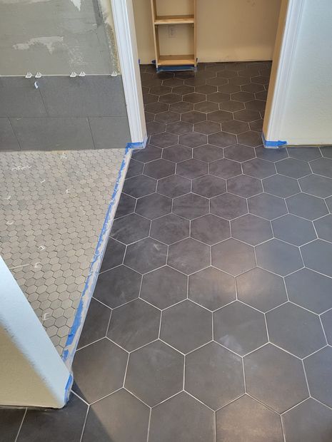 Hallway with dark hexagon tile flooring, adjacent speckled carpet, and open doorways with blue tape edges
