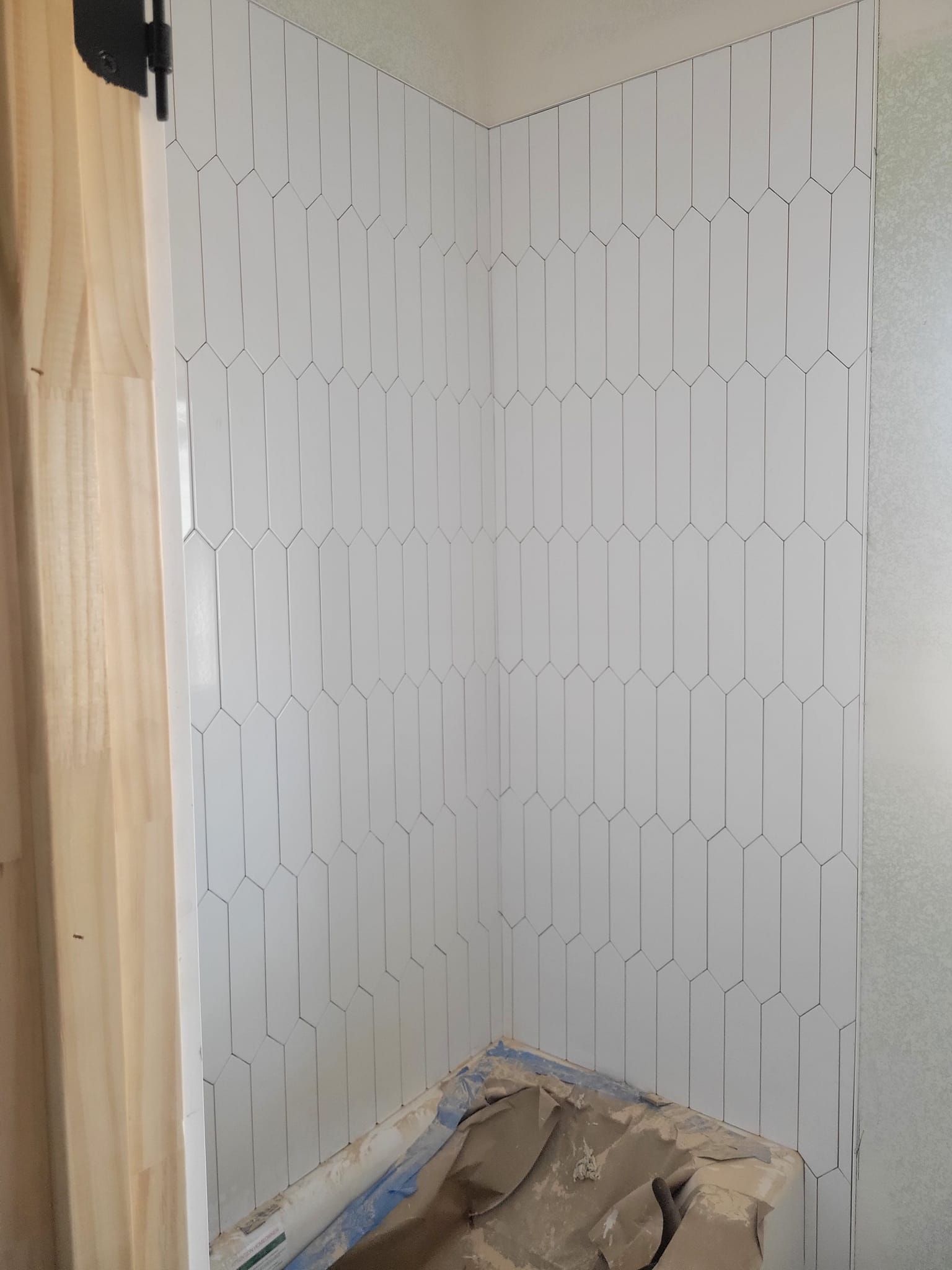 Unfinished bathroom corner with white wall tiles and exposed floor materials near the shower area