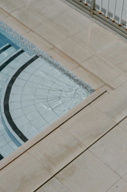 Curved glass skylight set into a beige stone walkway beside a metal railing