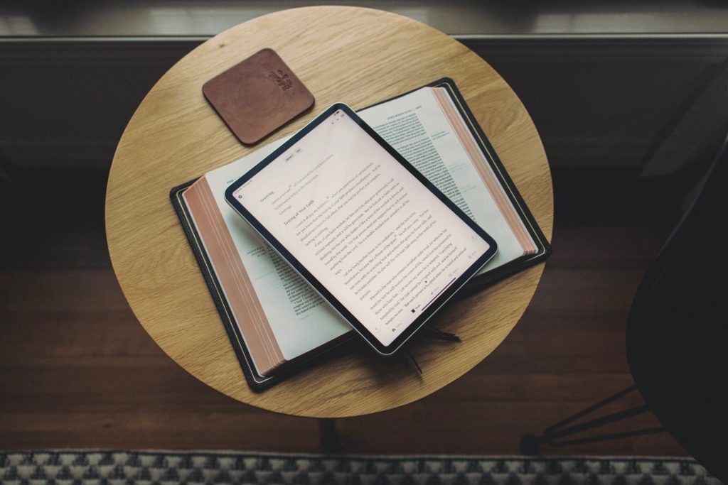 EReader on a small wooden table next to a coaster and the corner of a dark chair.