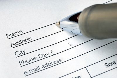 Close-up of a pen writing on a form with fields for name, address, and contact information.