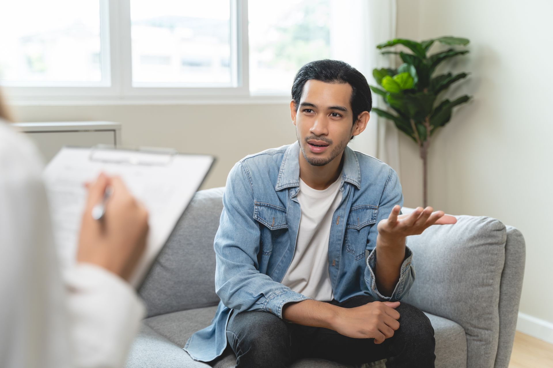 Person speaking with a counselor in a bright living room, seated on a gray couch.