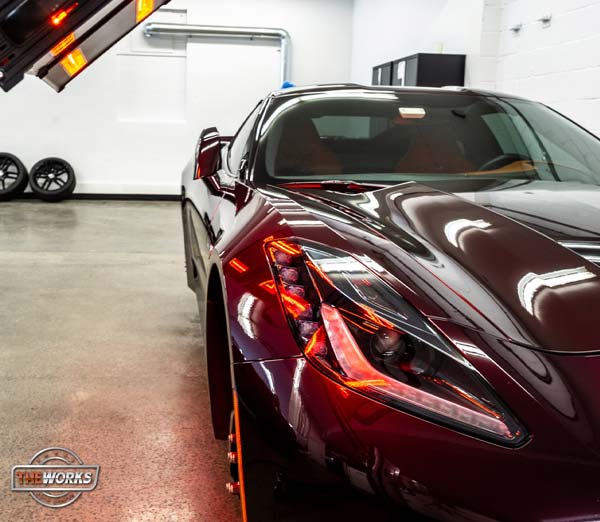 Burgundy sports car in a garage, illuminated headlights, shiny exterior.