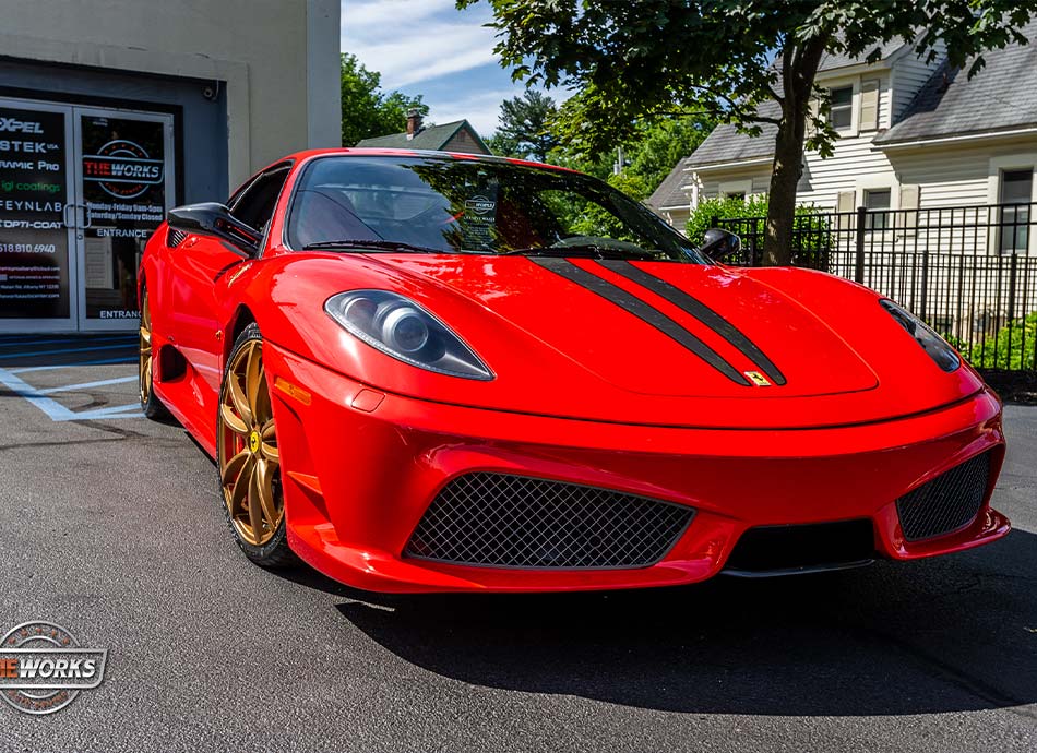 Red Ferrari sports car parked in front of a building with gold rims and black racing stripes.