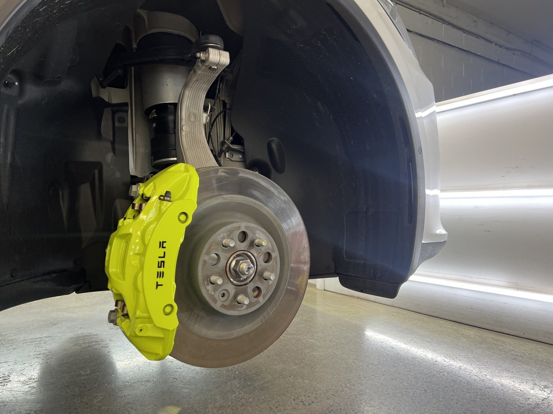 A tesla model s with yellow brake calipers is parked in a garage.