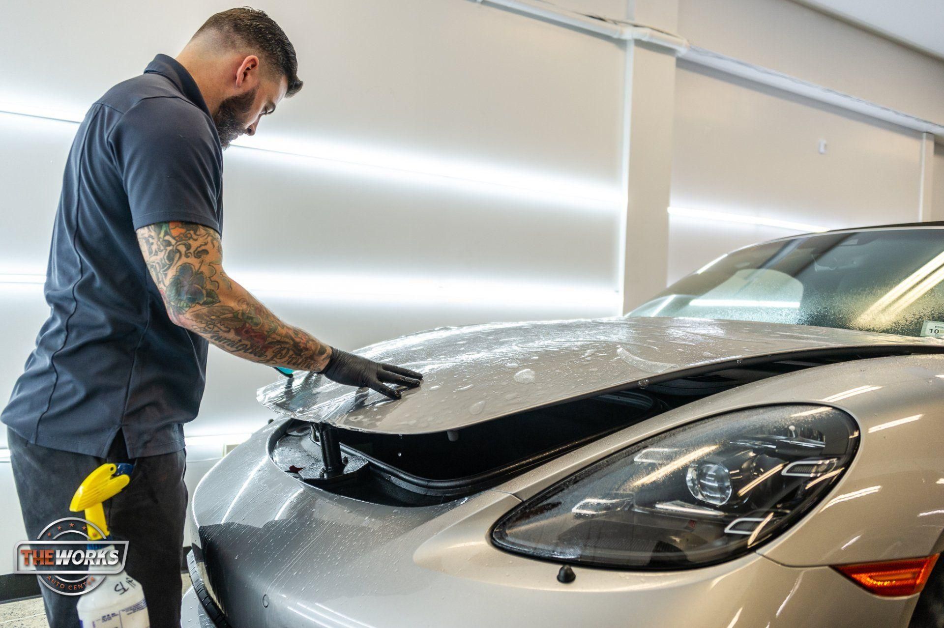 Technician polishing the hood of a silver sports car in a bright auto shop