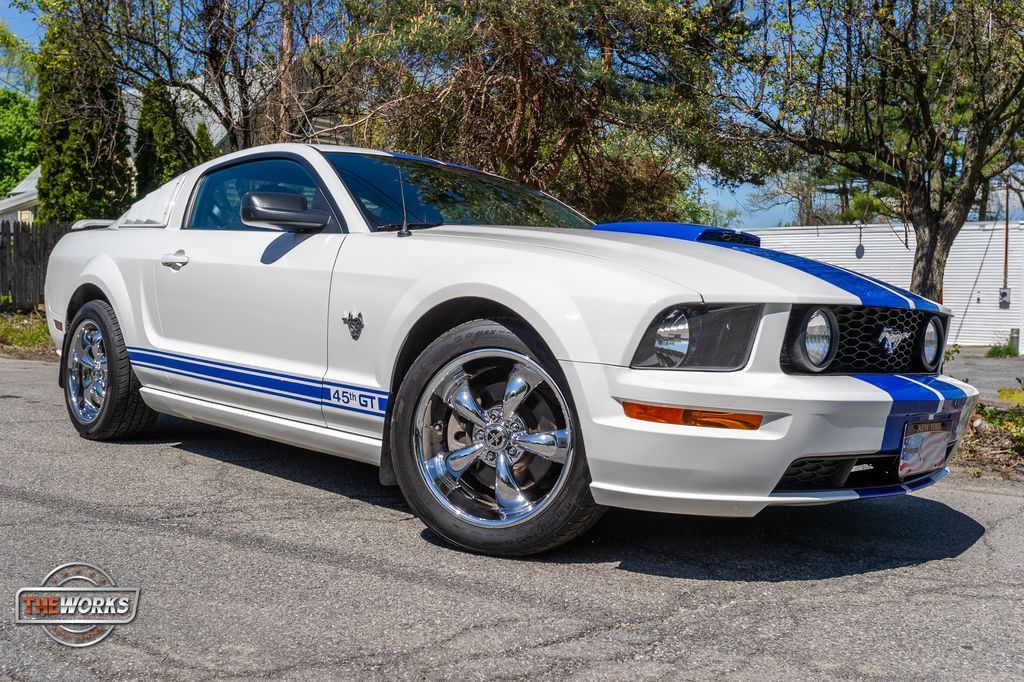 White Ford Mustang with blue racing stripes and chrome wheels parked on an asphalt lot.