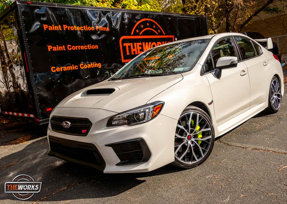 A white subaru wrx sti is parked in front of a black trailer.