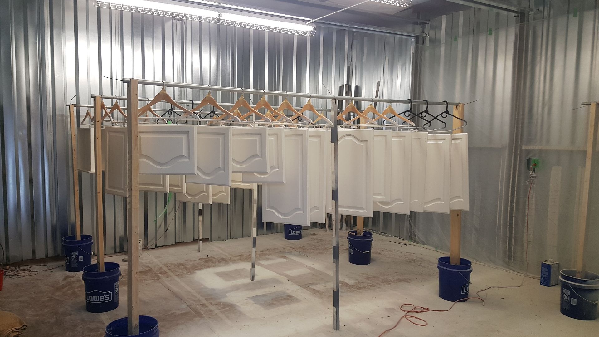 Industrial paint booth with hanging white panels and blue buckets on a concrete floor