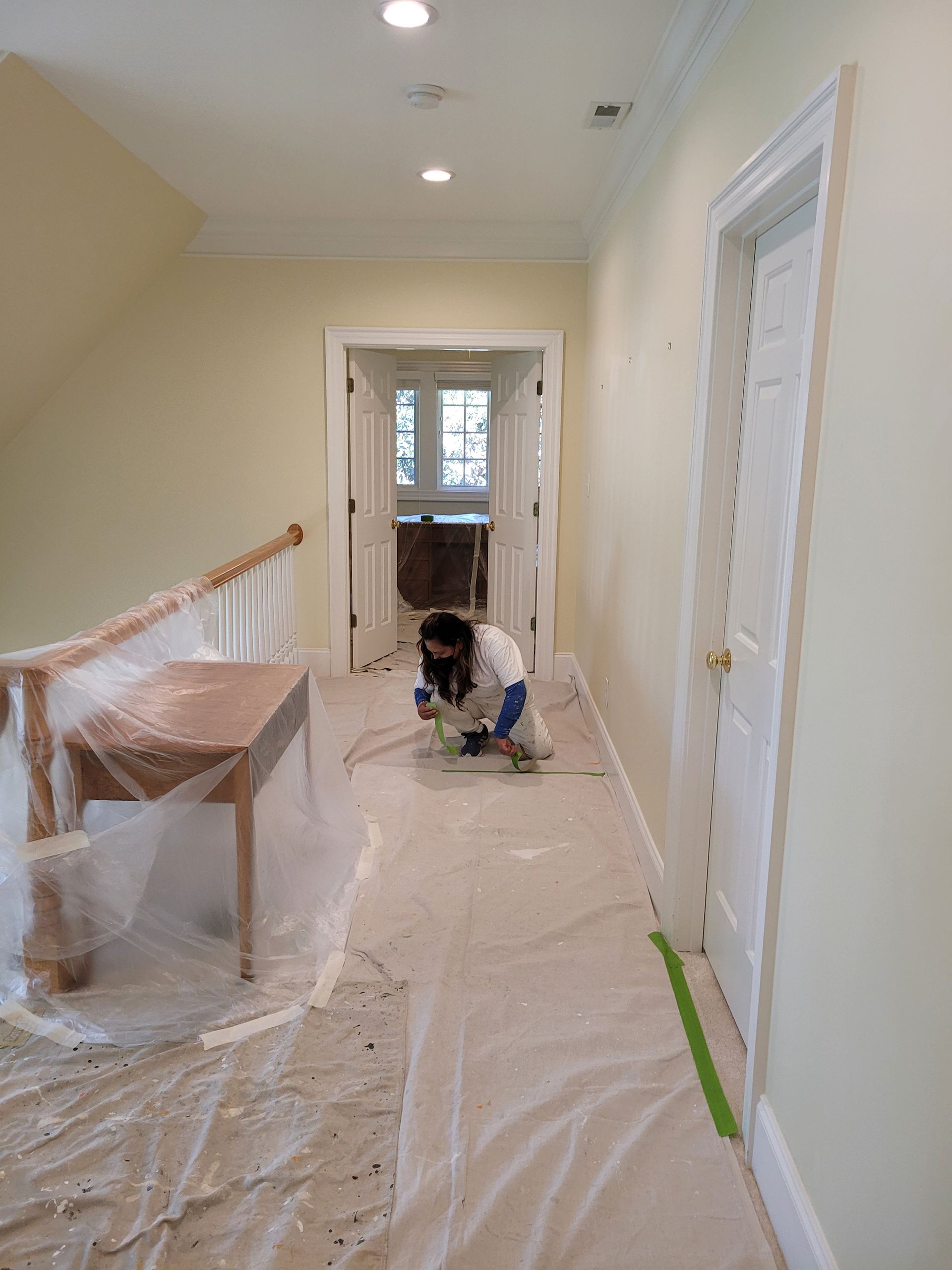 Hallway under renovation with a worker kneeling on the floor, plastic sheeting, and a bench along the wall