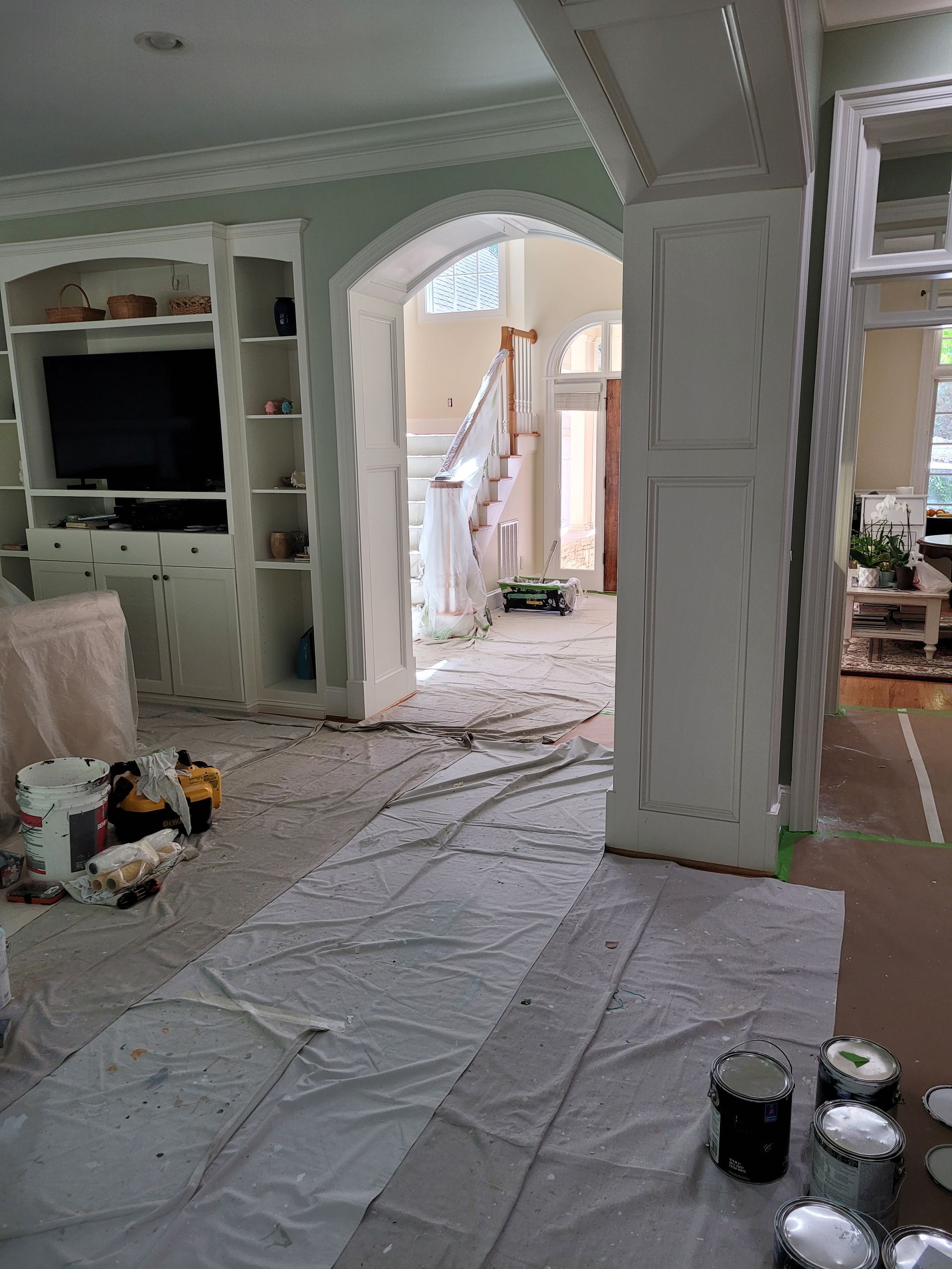 Renovated living room with plastic-covered floor, white built-ins, and open archway to a hallway with ladder and tools