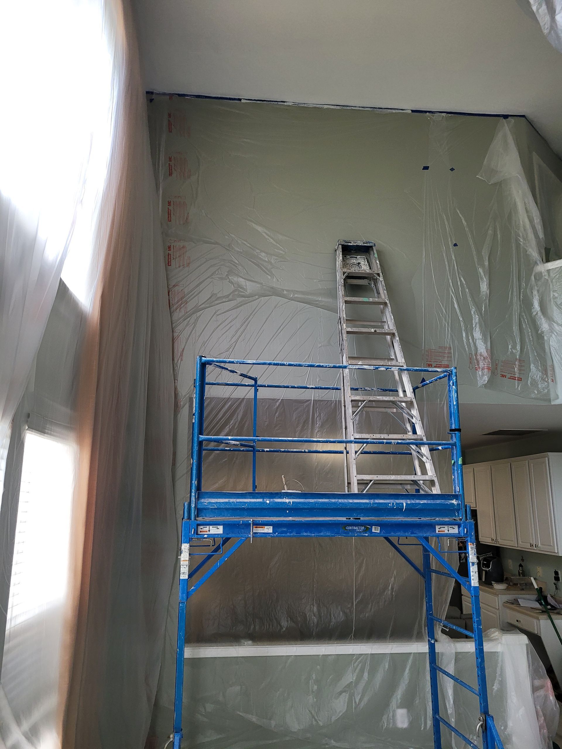 Blue scissor lift and ladder in a large unfinished interior with wet gray walls.