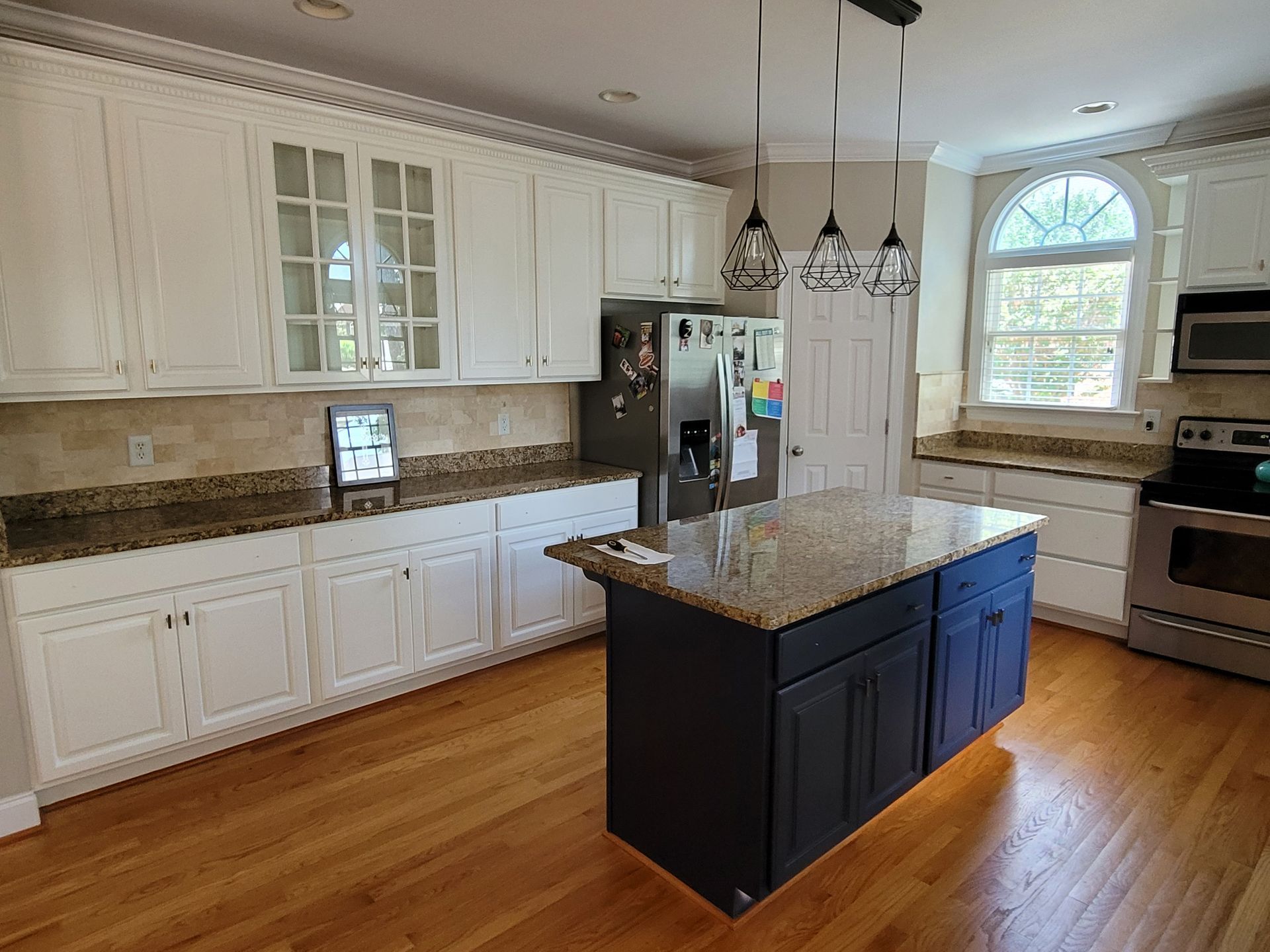 Bright kitchen with white cabinets, granite island, hardwood floors, stainless appliances, and pendant lights.