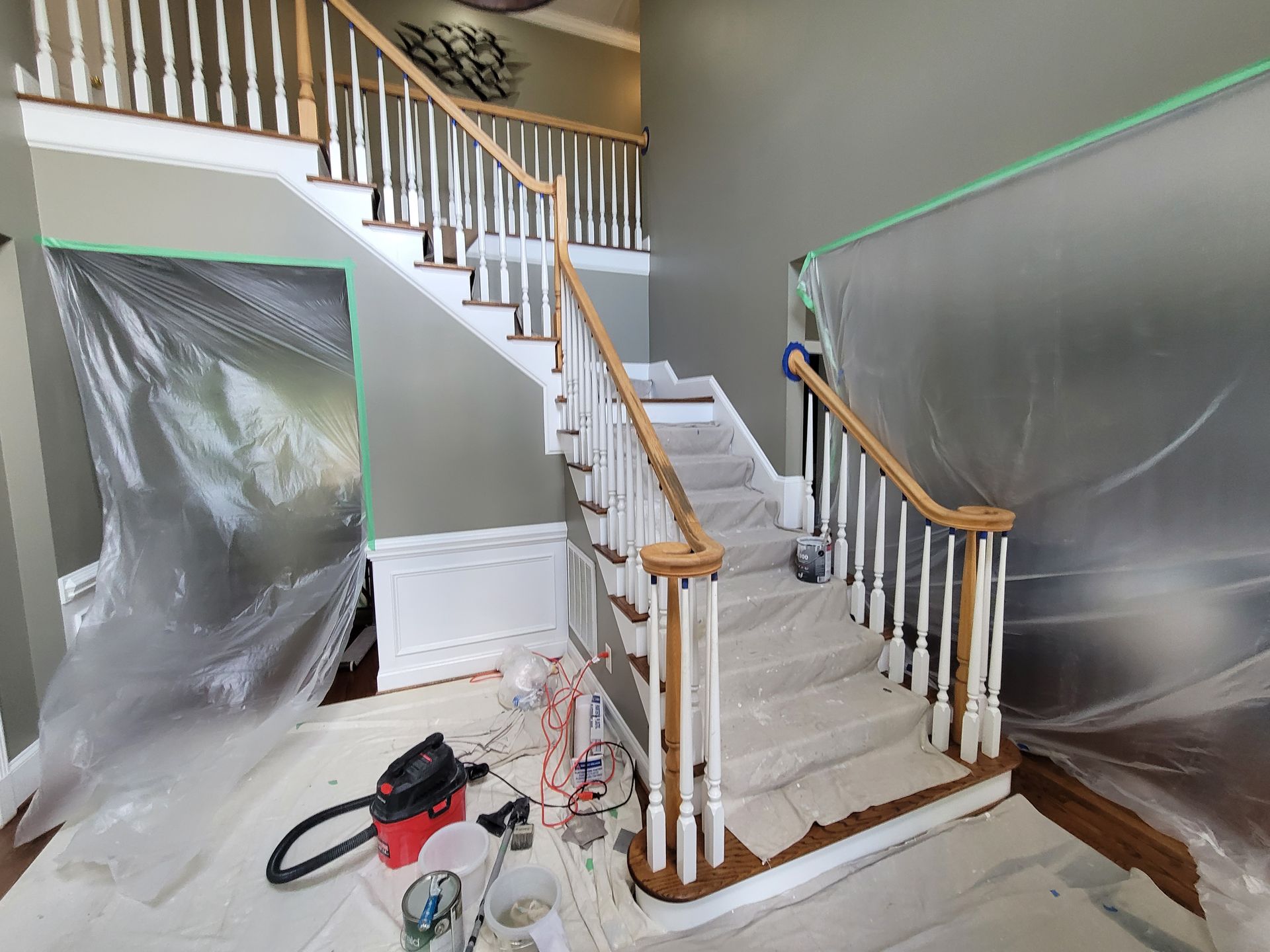 Staircase under renovation, wrapped in plastic sheeting with tools on the floor and green painter’s tape.