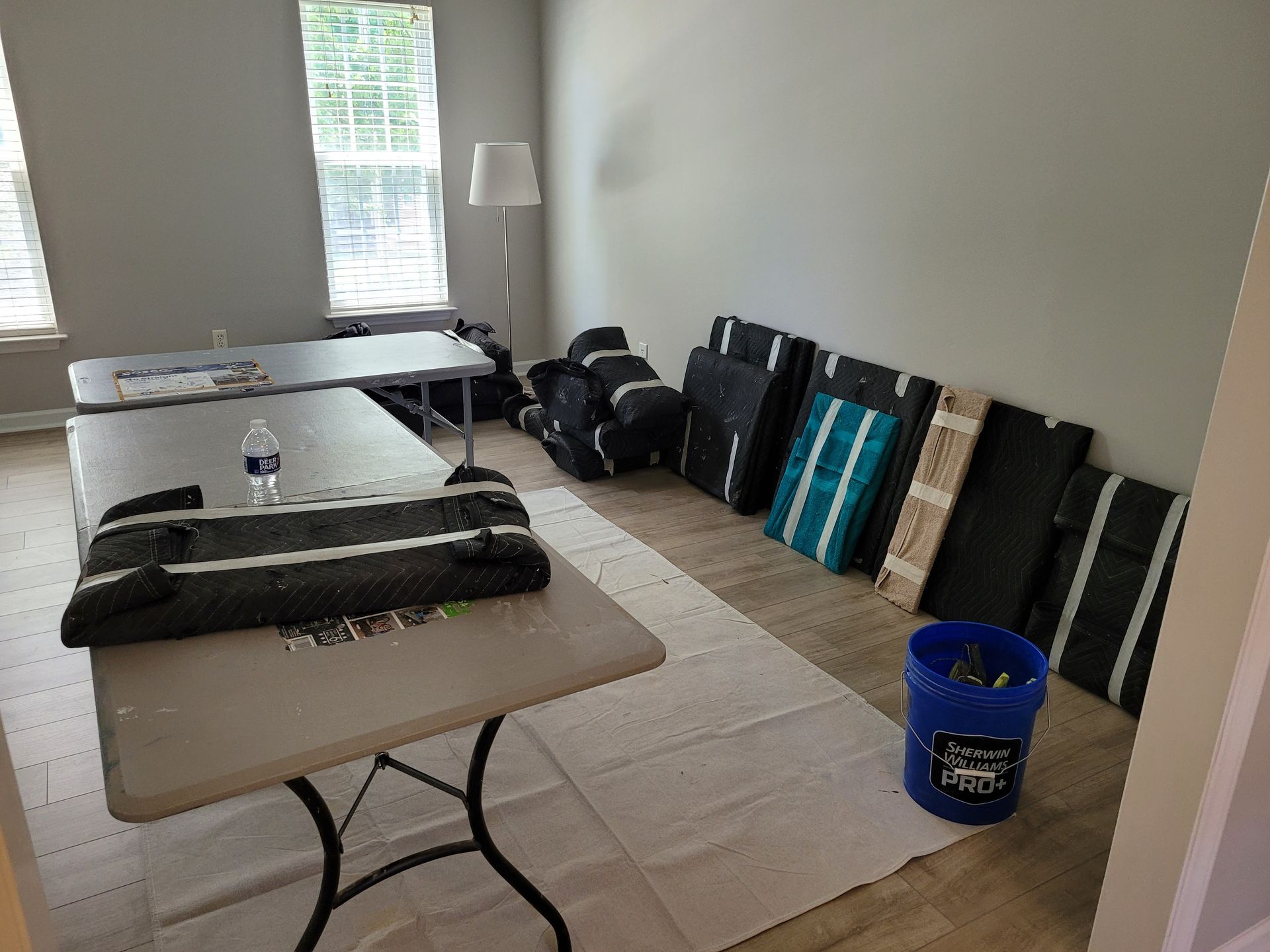 Folded tables and mats stacked along a wall in a plain room, with a blue basket on the floor.