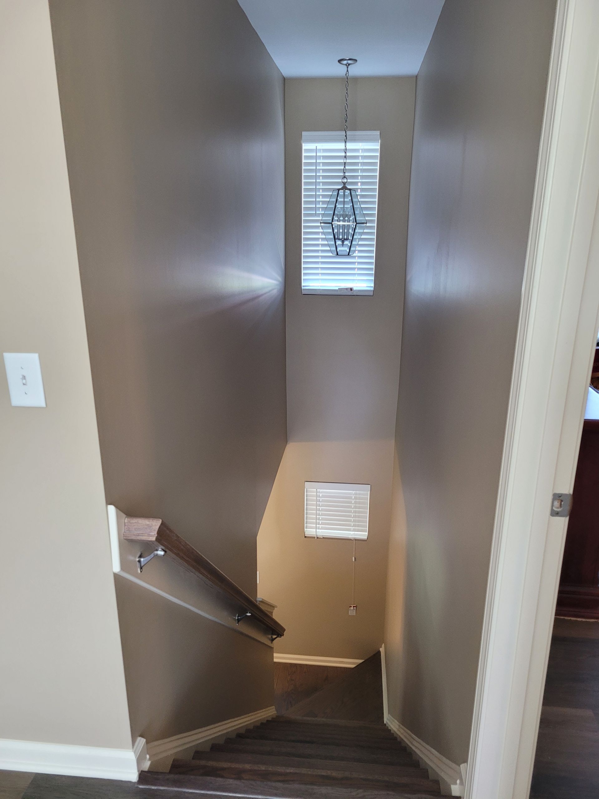 Stairwell with beige walls and dark carpet leading down to a small window at the landing.