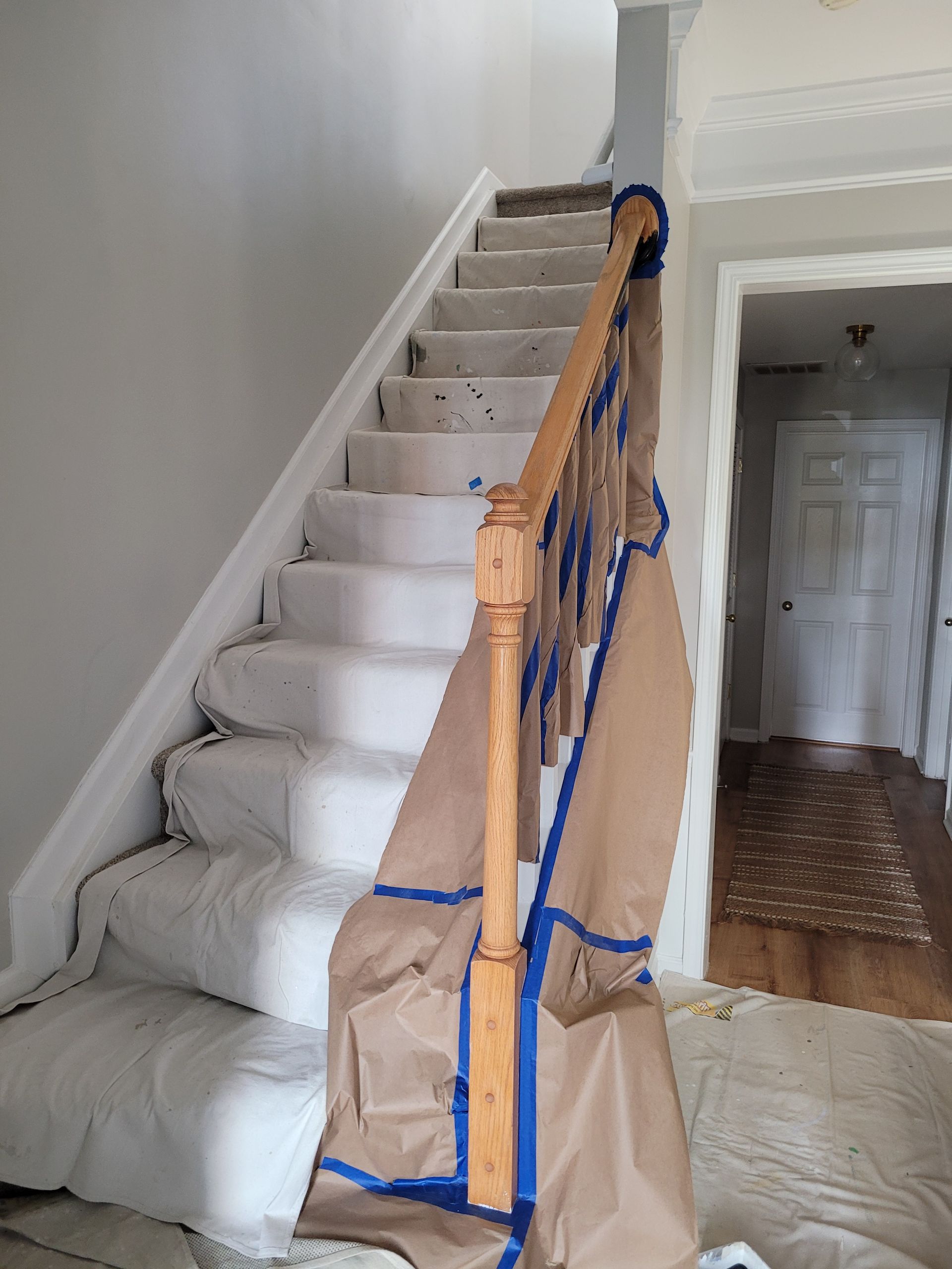 Staircase with white-wrapped steps, blue tape, and paper-covered banister in a house interior