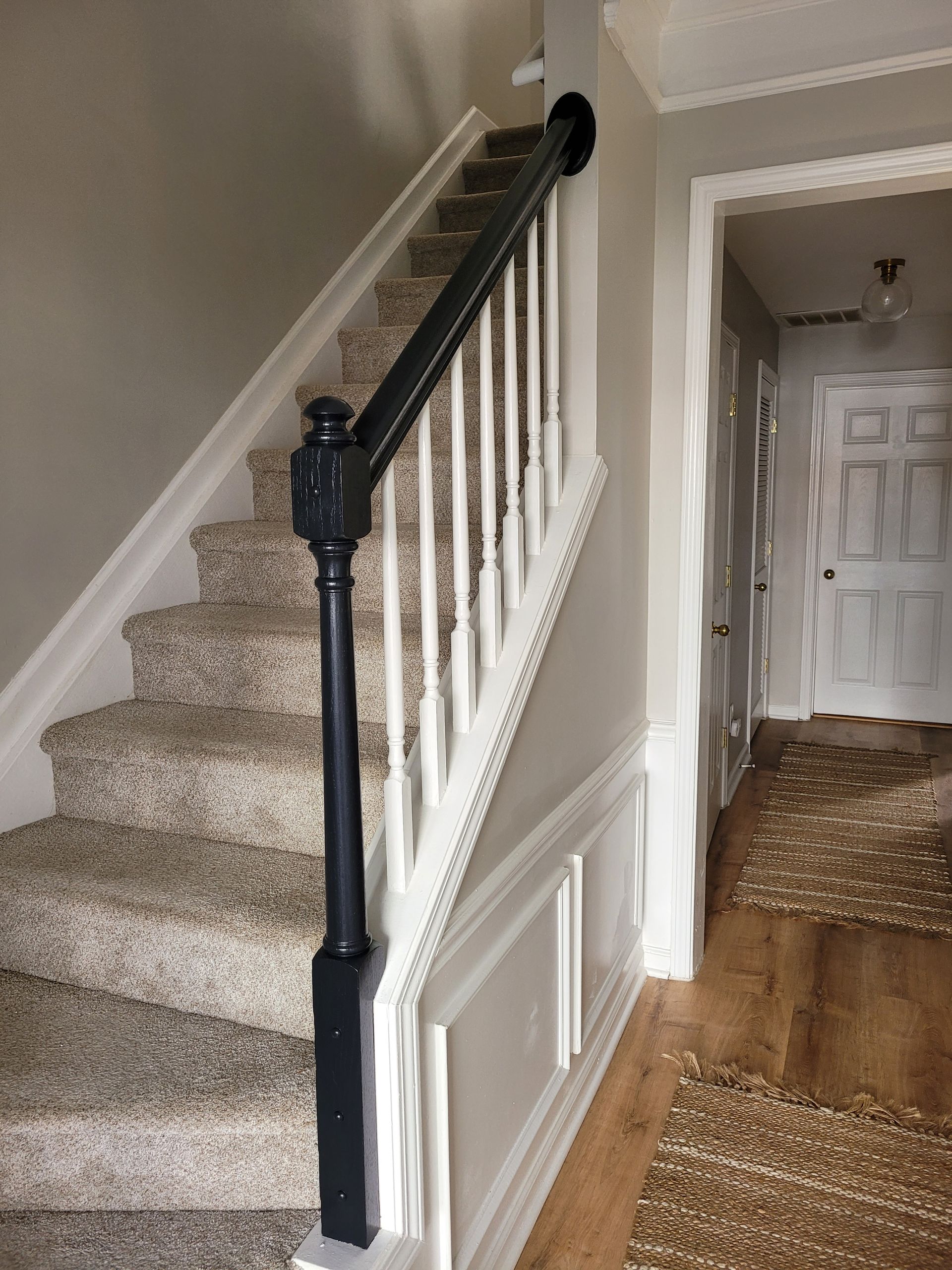 Carpeted staircase with black handrail beside a hallway and white front door