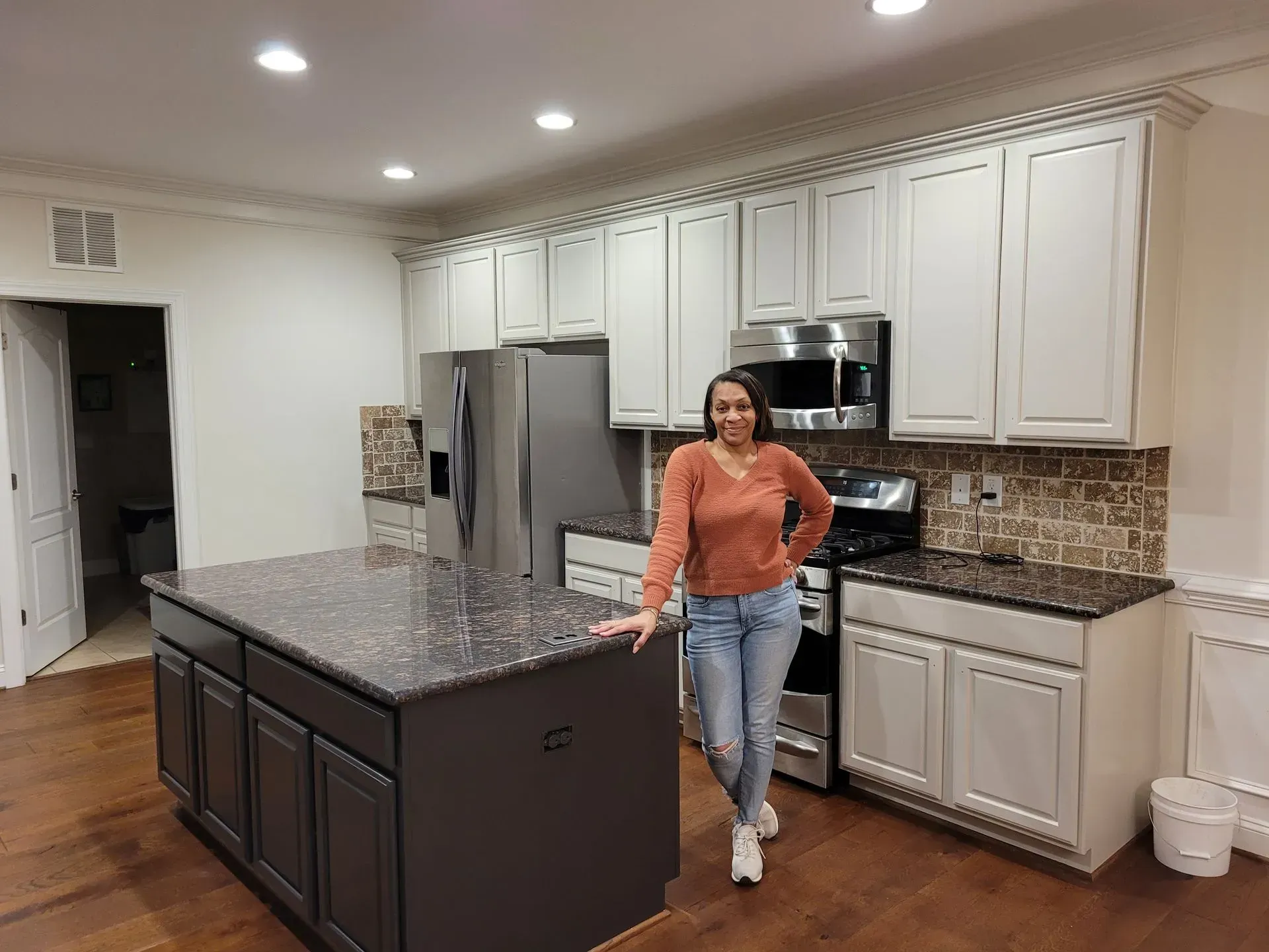 Woman standing in a modern kitchen beside a granite island and stainless steel appliances