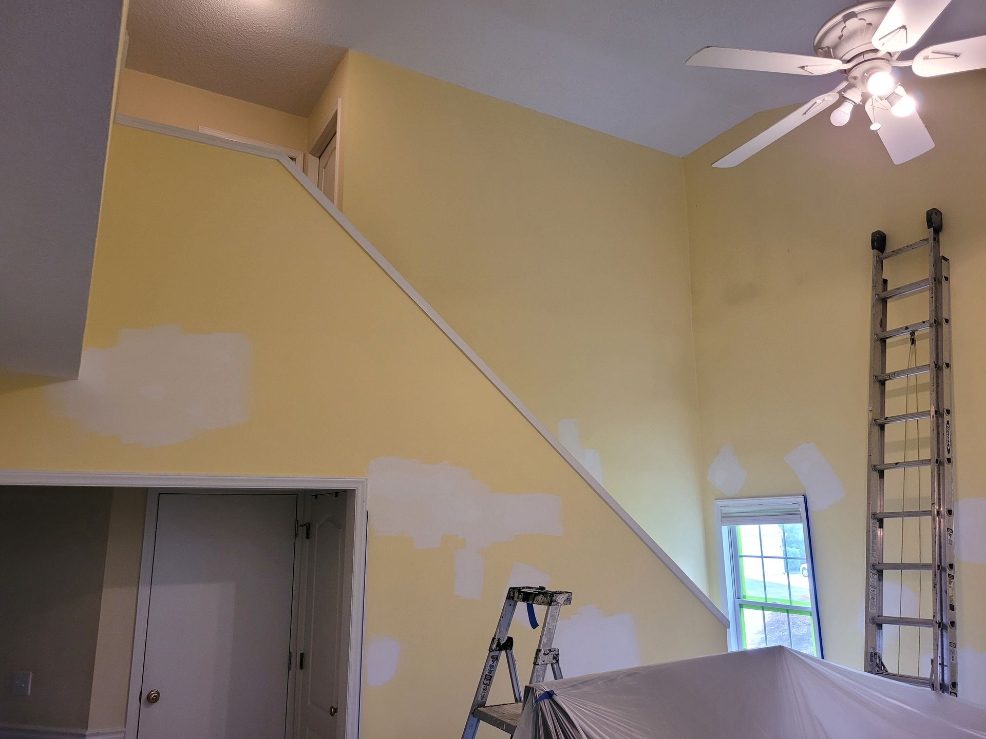 Interior room with yellow walls, ladders, and paint patches, suggesting ongoing renovation or repair