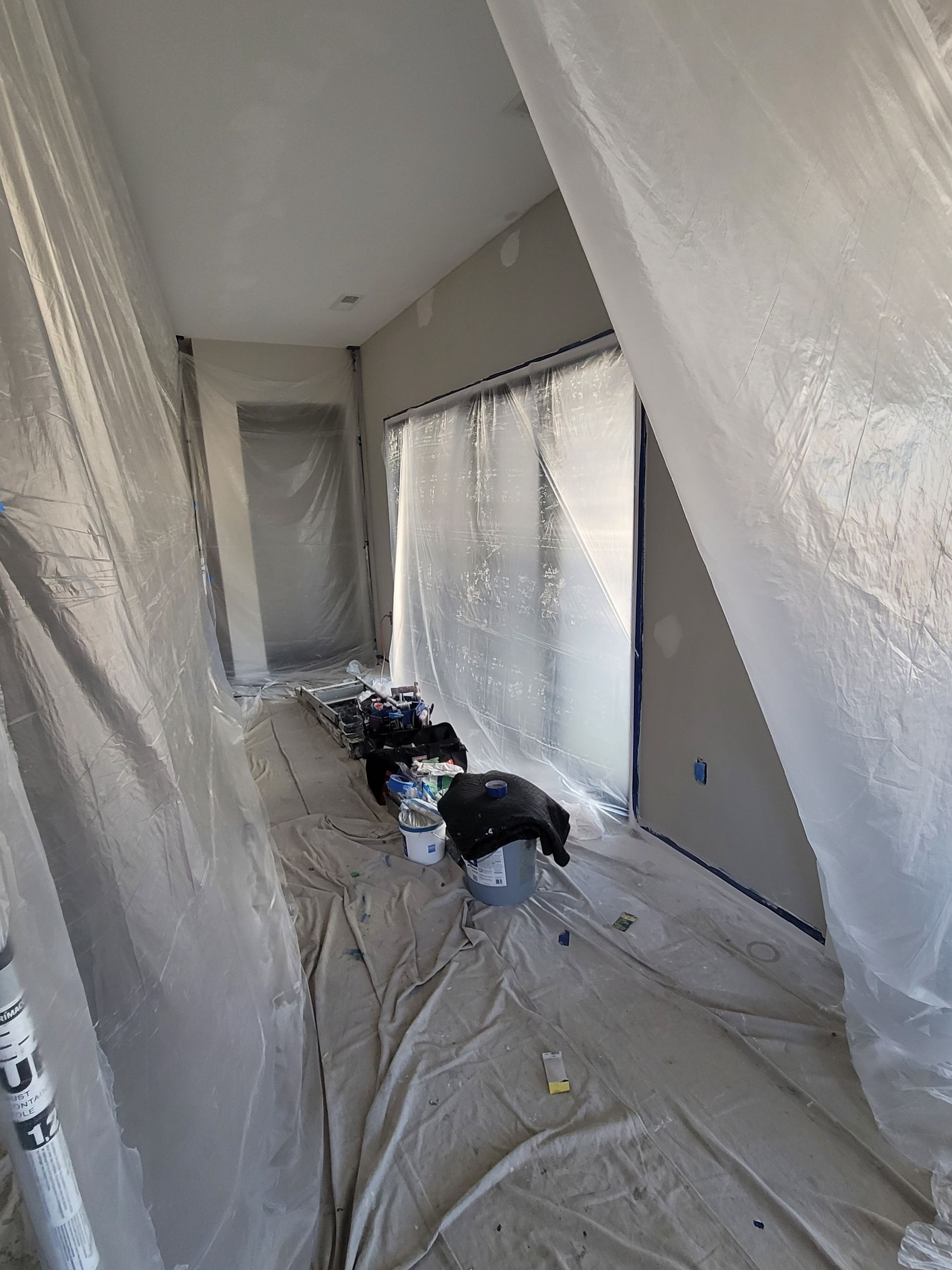 Hallway under renovation, walls and floor covered in plastic sheeting, with tools and supplies along the side.