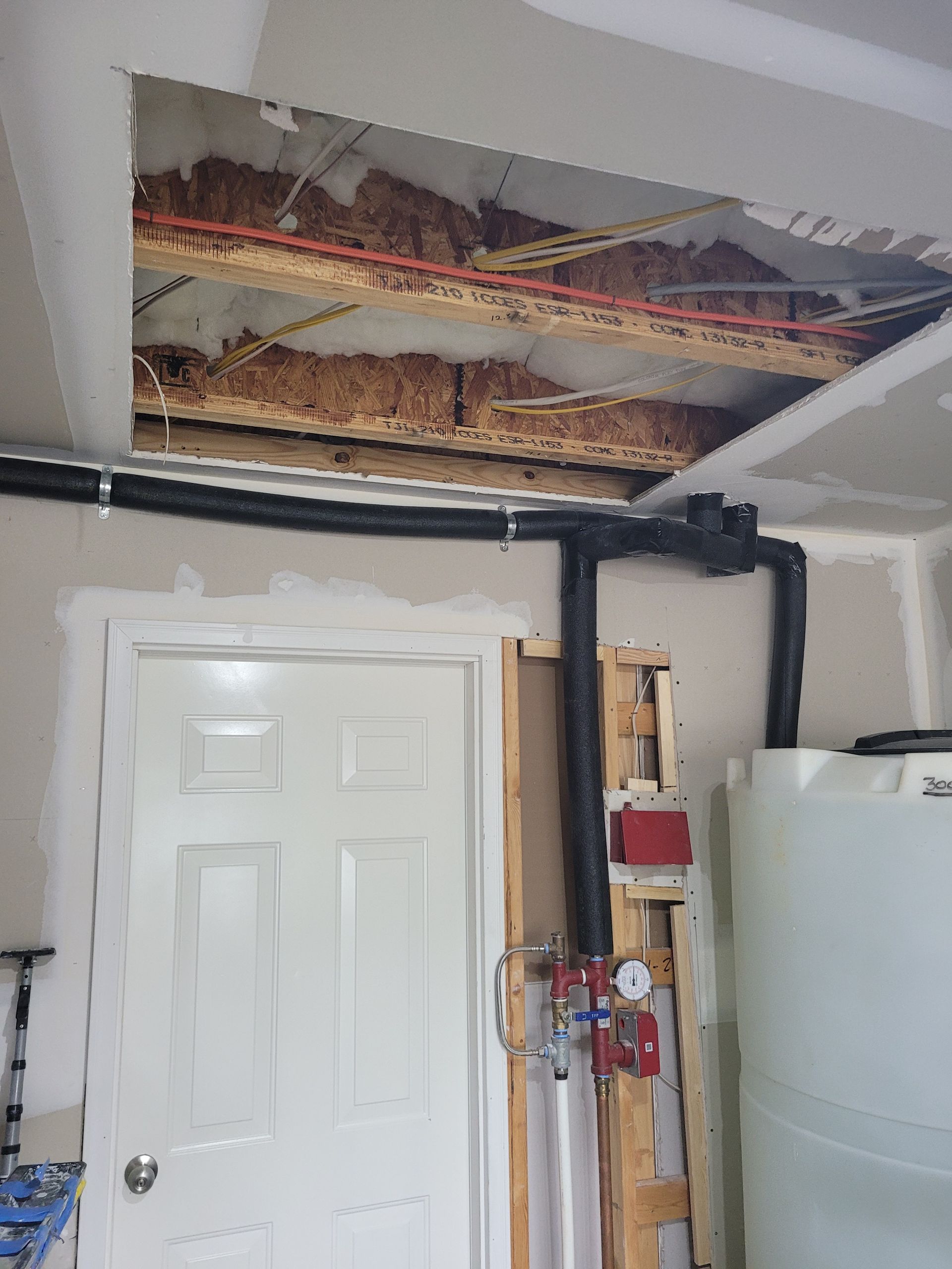 Garage interior with a damaged ceiling exposing insulation above a white door and water heater