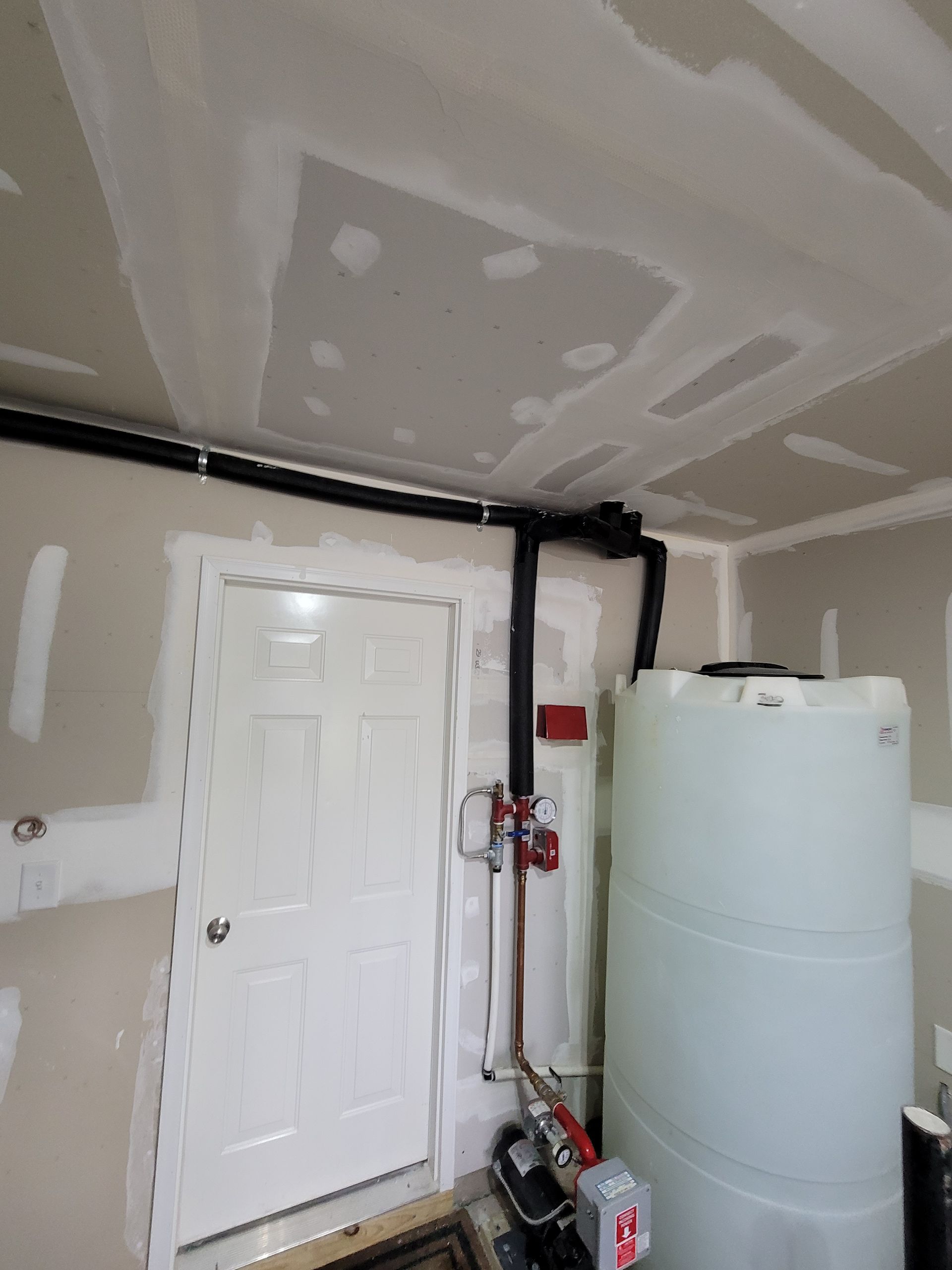 Garage interior with utility tank, pipes, and a white door against unfinished drywall.