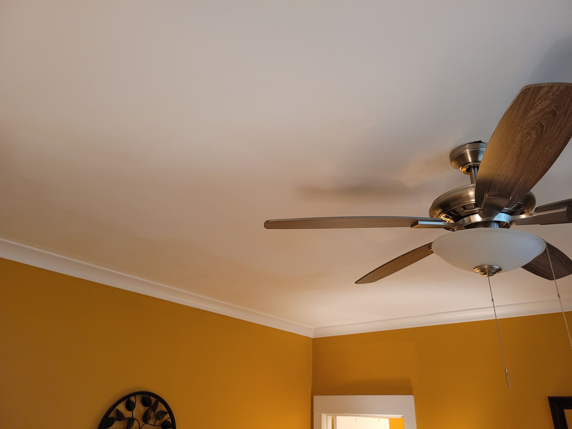 Ceiling fan on a beige ceiling above mustard-yellow walls and a wall clock.